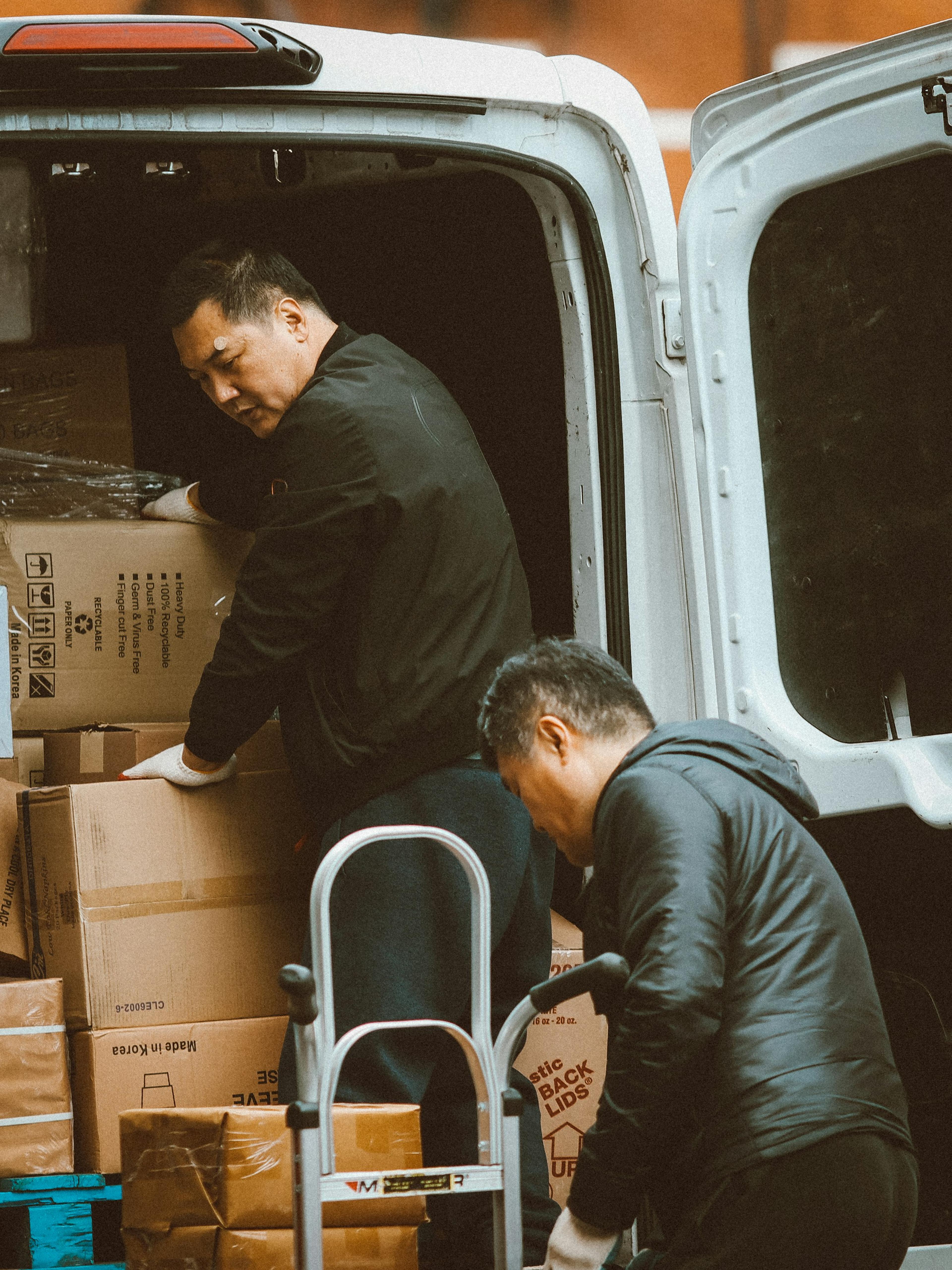 Two delivery workers unloading heavy boxes from a van onto a hand truck, the lifting behind many delivery driver workers’ comp claims