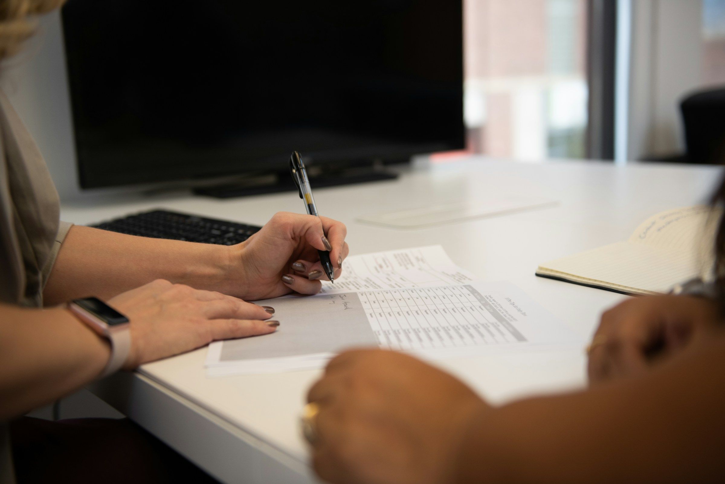 Mano firmando un formulario frente a otra persona, un paso que conviene dar solo después de revisar un acuerdo de compensación laboral