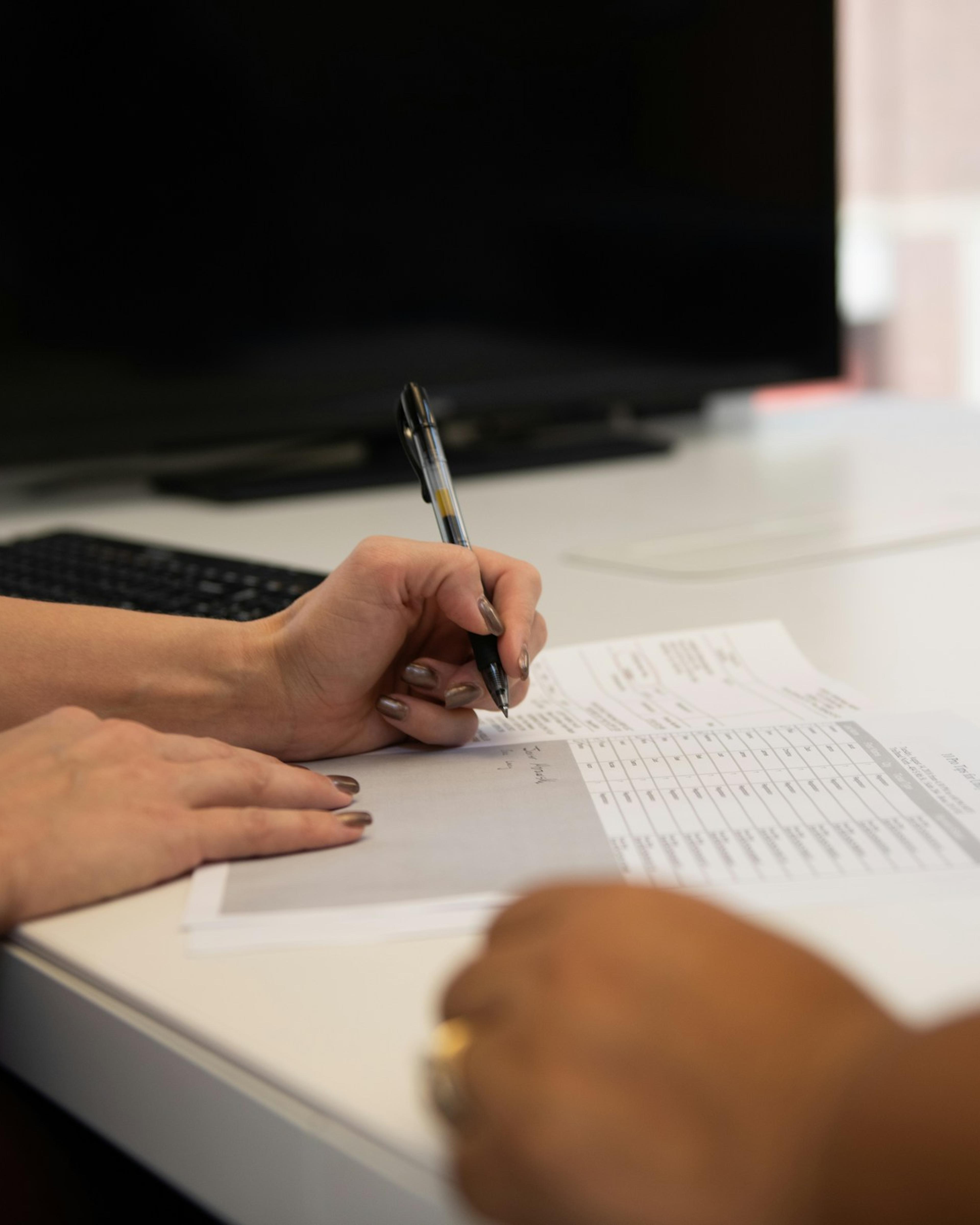 Mano firmando un formulario frente a otra persona, un paso que conviene dar solo después de revisar un acuerdo de compensación laboral