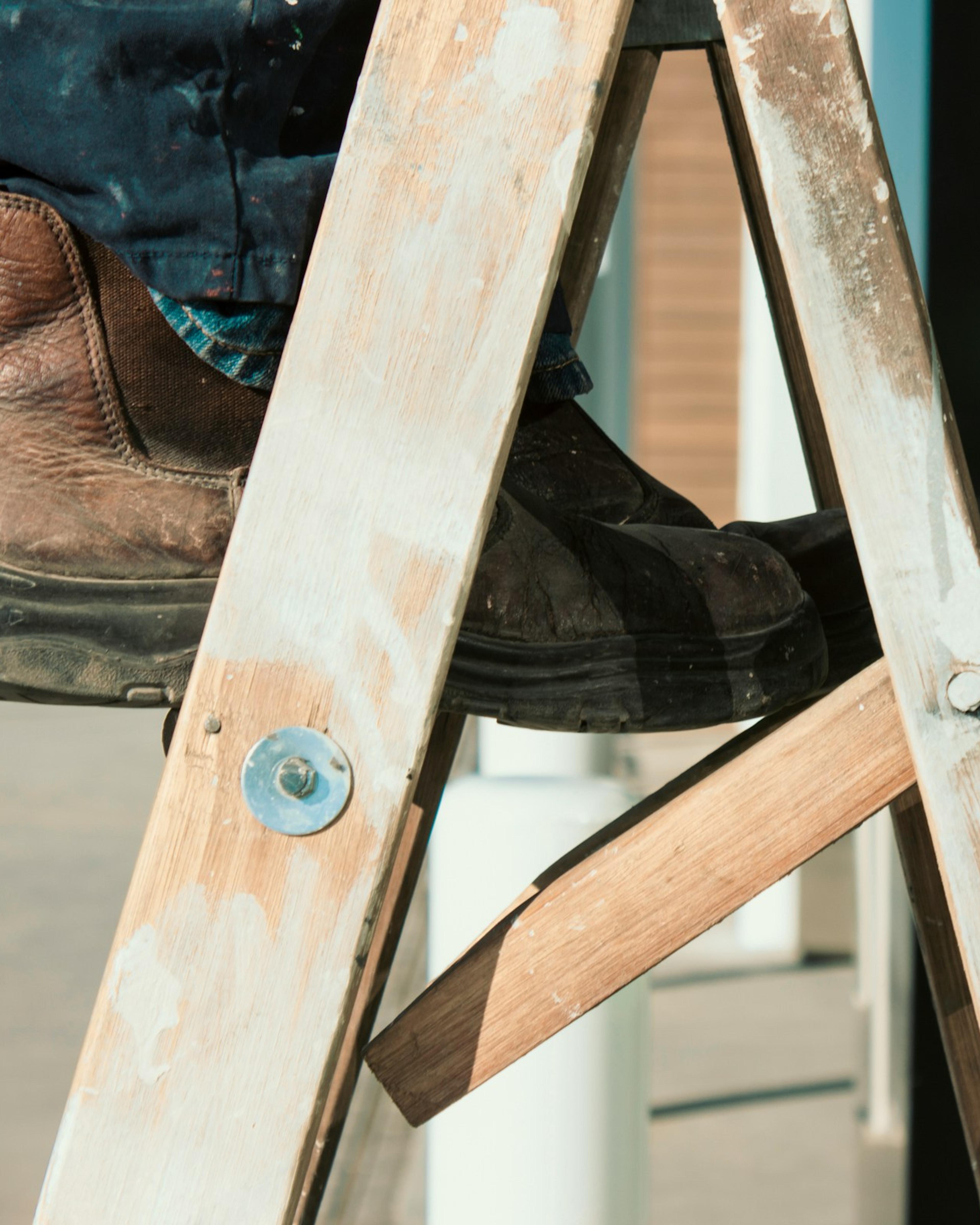 Work boot on the step of a worn wooden stepladder; workers’ comp can cover treatment after a fall at work from a ladder