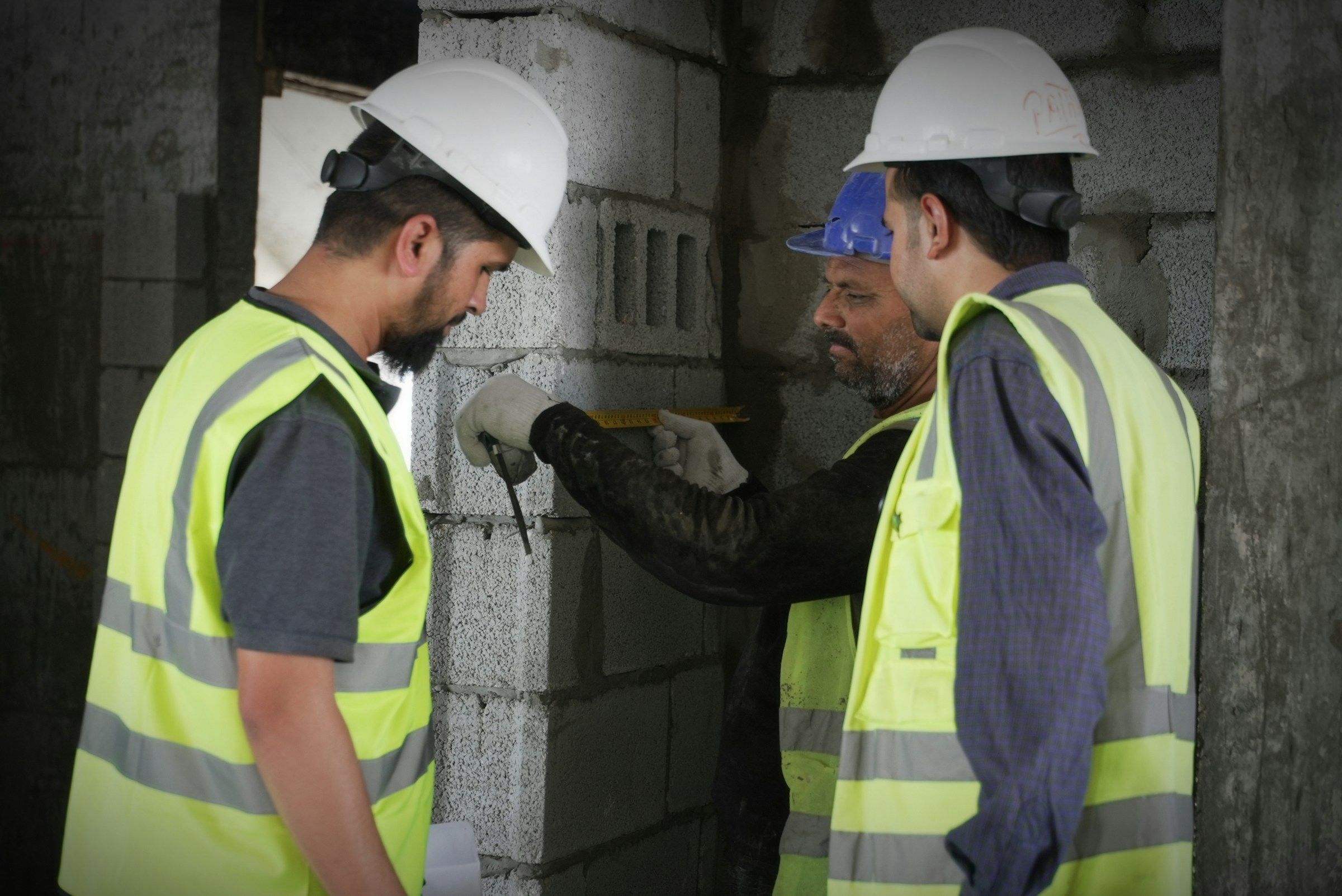 Construction crew in high-visibility vests measuring a concrete wall