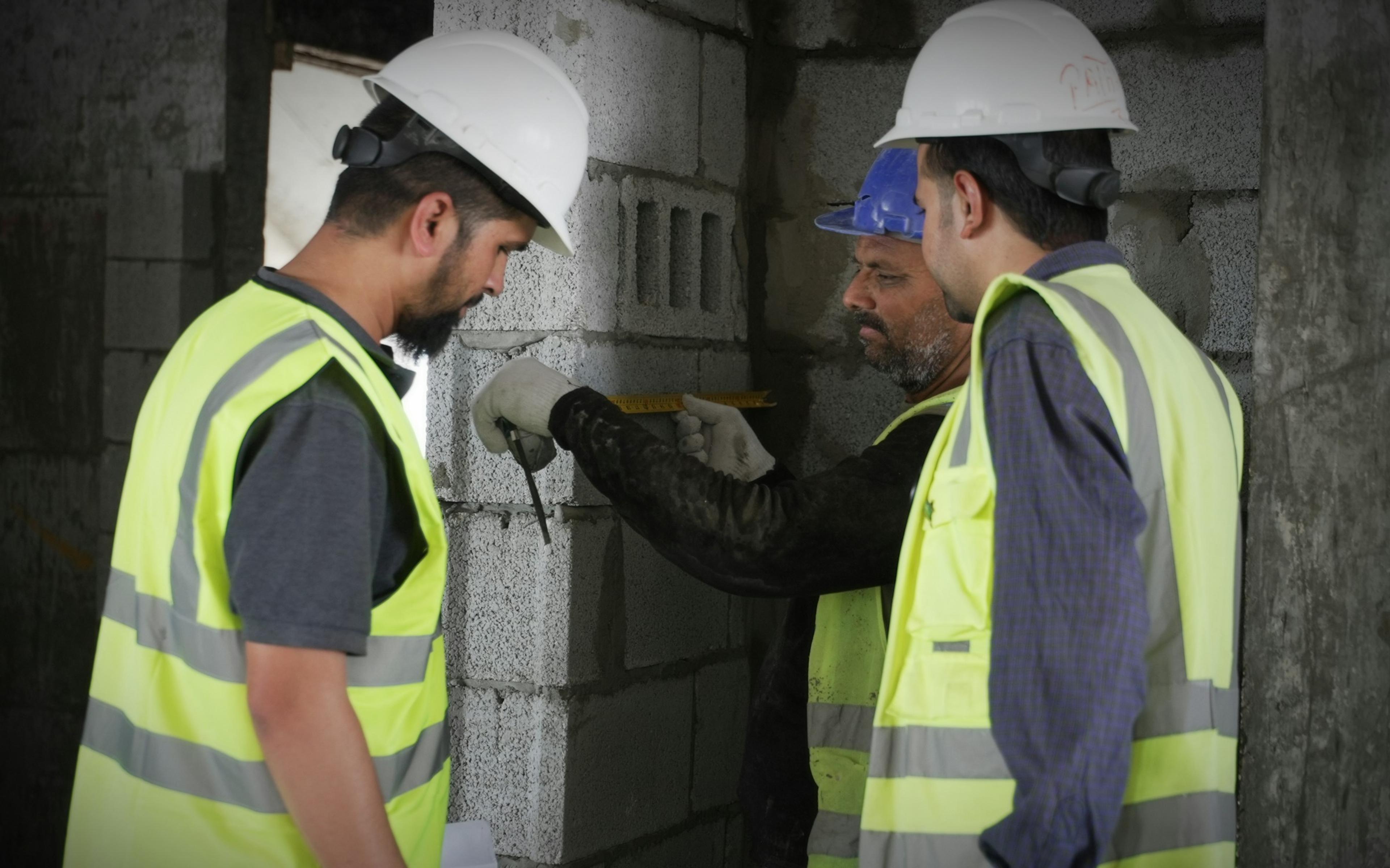 Construction crew in high-visibility vests measuring a concrete wall