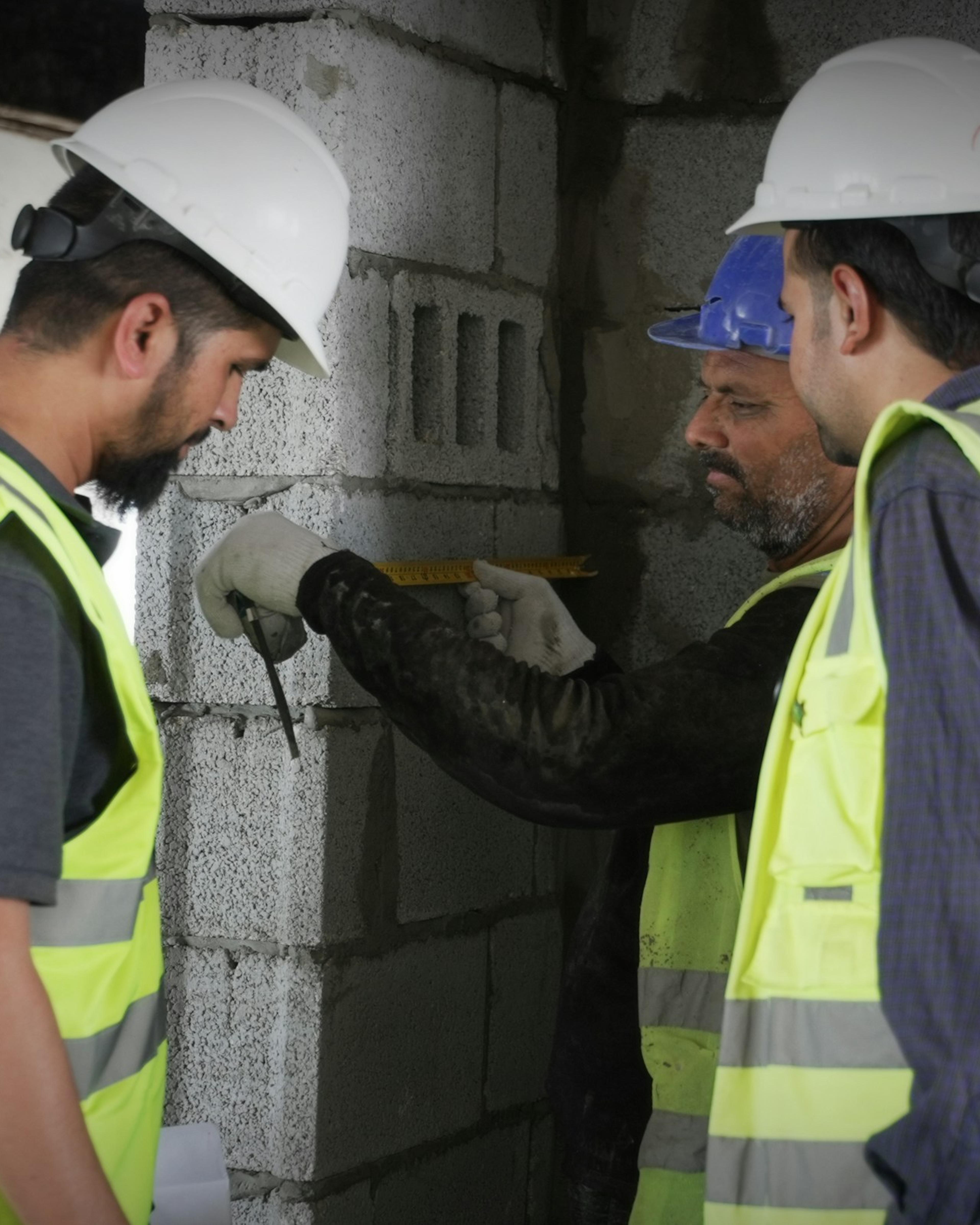 Construction crew in high-visibility vests measuring a concrete wall