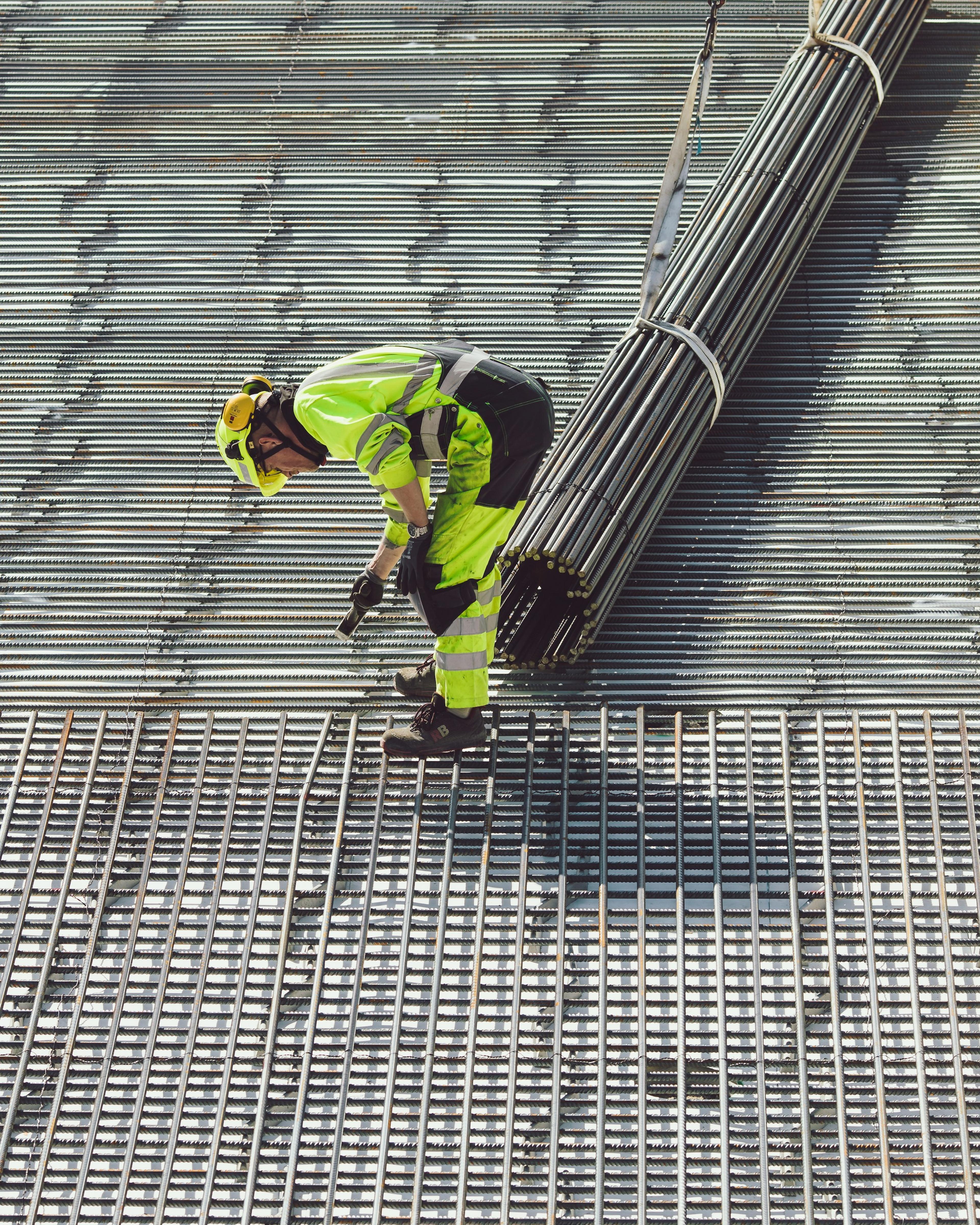 Trabajador inclinado sobre una malla de varilla junto a un paquete de acero colgado de una grúa, un trabajo pesado cubierto por la compensación laboral