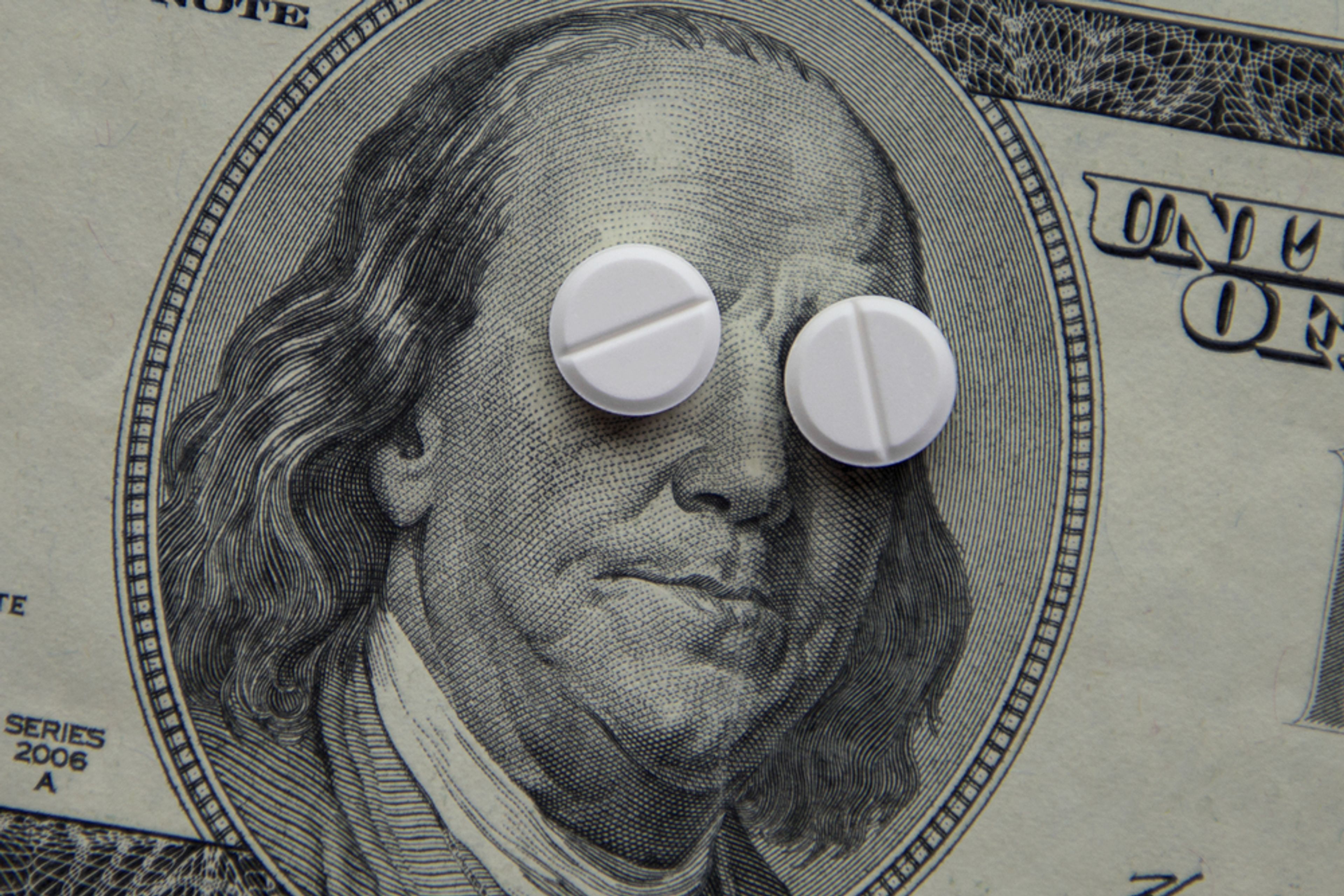 A photo of a US Dollar bill with two pills laid over the eyes of the Presidential portrait