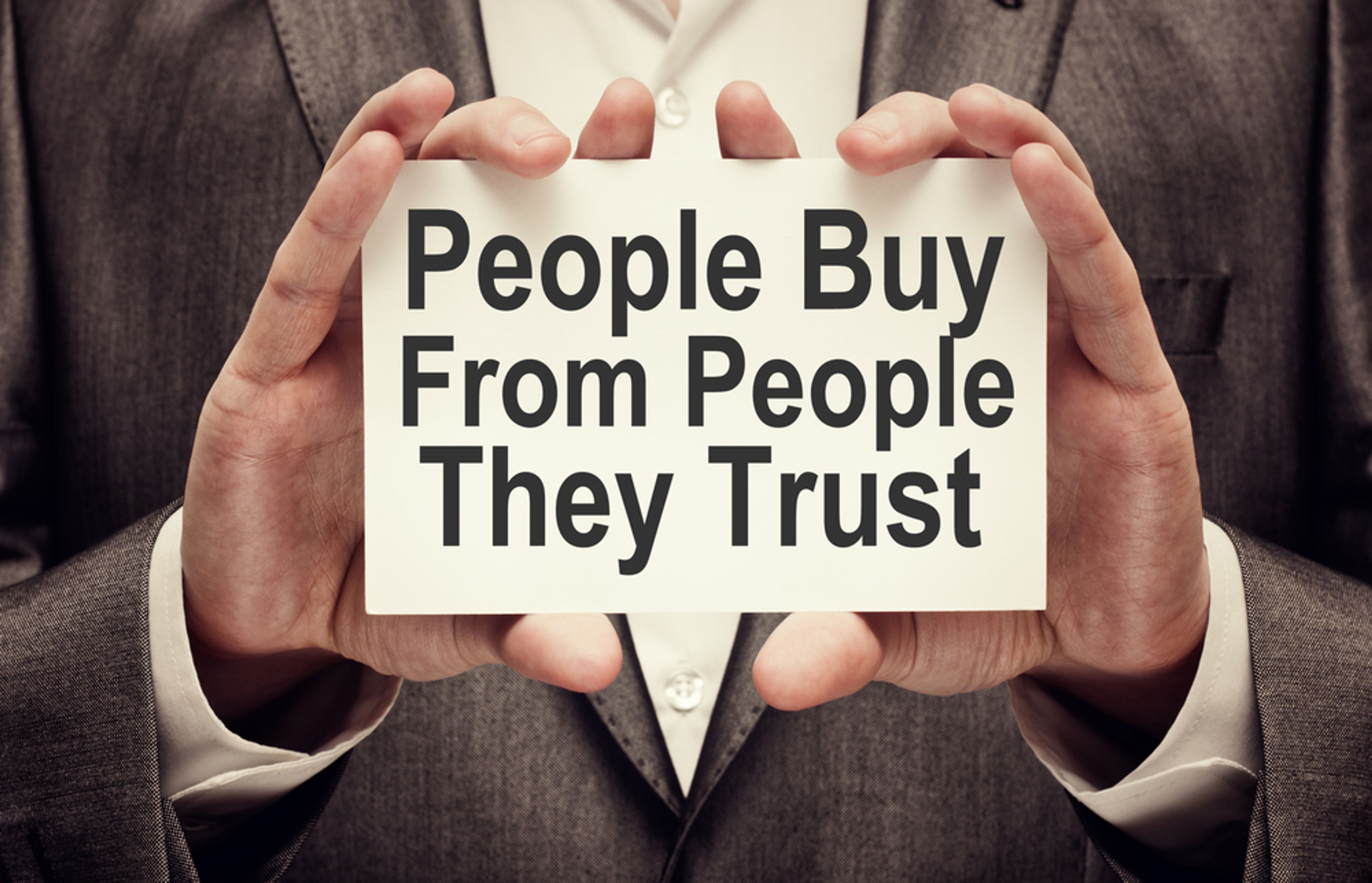 An image of a person holding a sign that says 'People buy from people they trust'