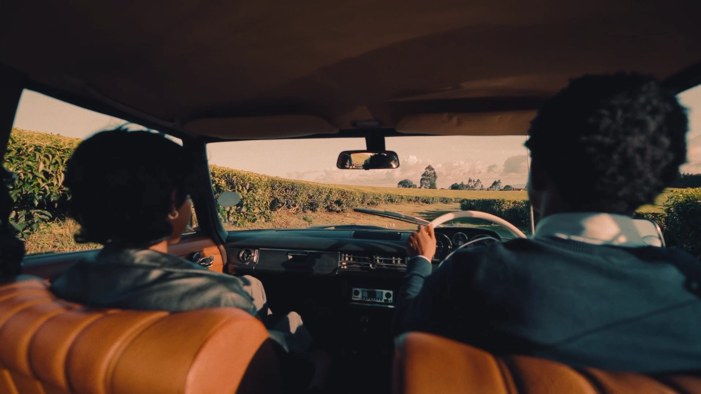 Couple inside a tan-leather vintage car with tea fields beyond