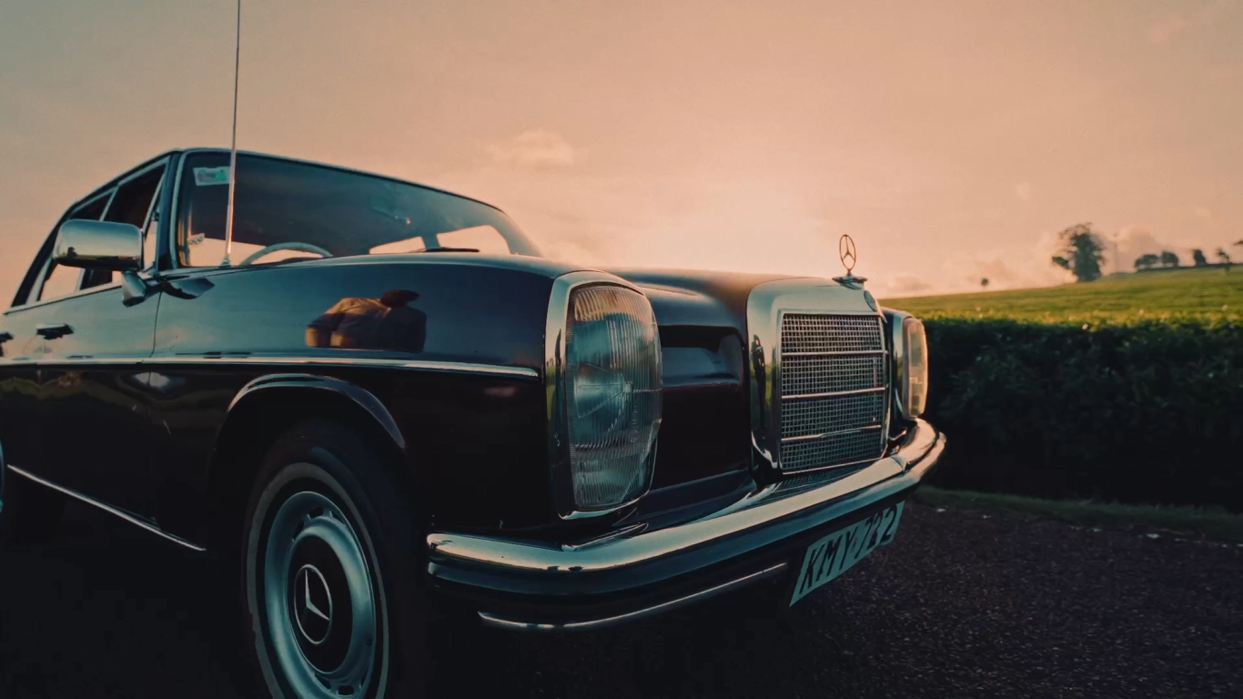 Black vintage Mercedes parked by tea fields at sunset