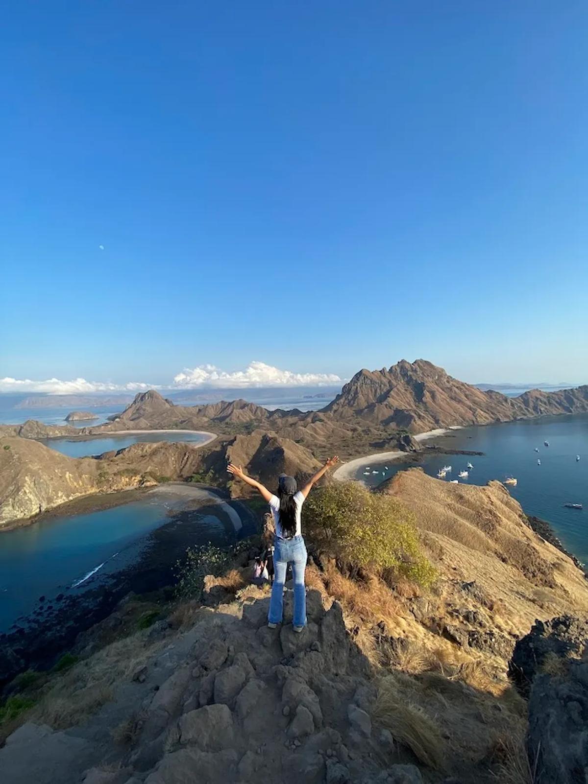 Wisatawan berdiri di puncak Pulau Padar dengan pemandangan teluk dan pegunungan di Taman Nasional Komodo Labuan Bajo
