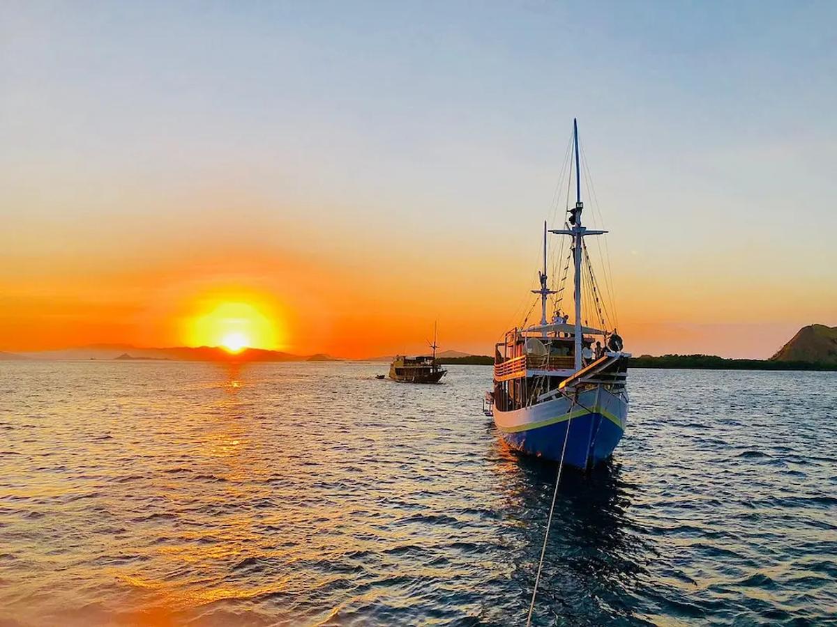 Kapal kayu tradisional di tengah laut tenang saat matahari terbenam keemasan dalam tur liveaboard Labuan Bajo
