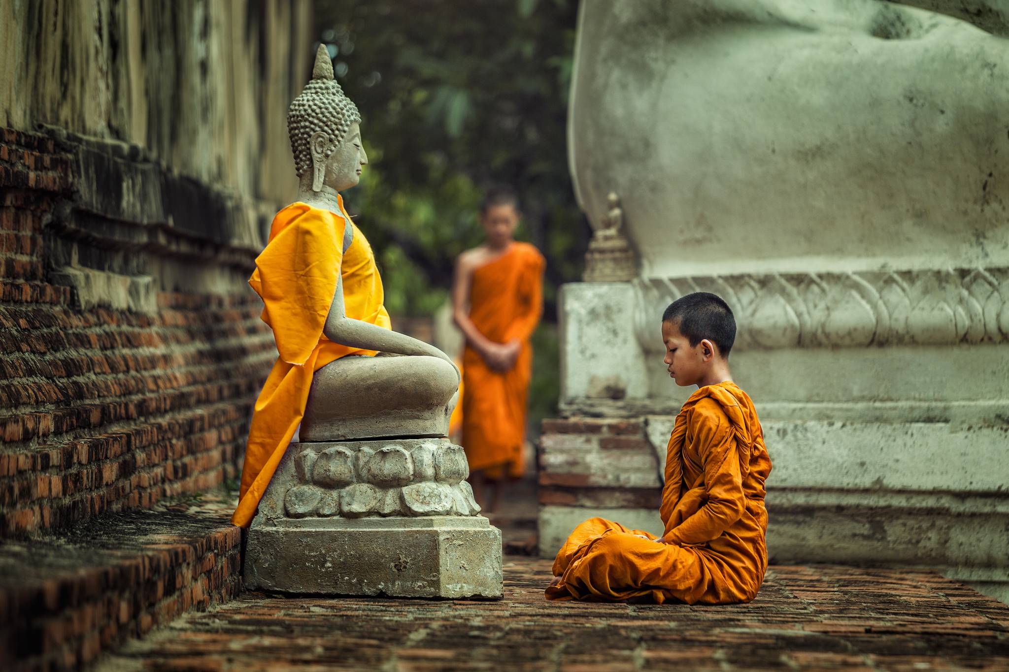 giovane monaco tibetano prega statua di buddha