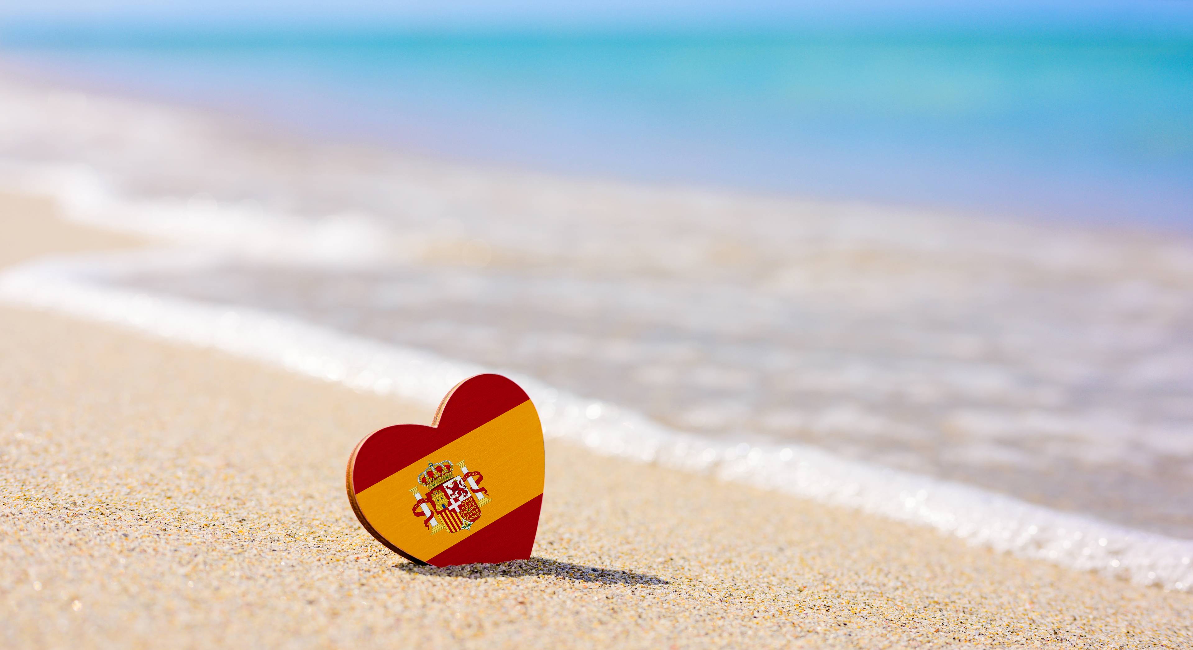 cuore con bandiera spagnola sulla sabbia in spiaggia con mare sullo sfondo