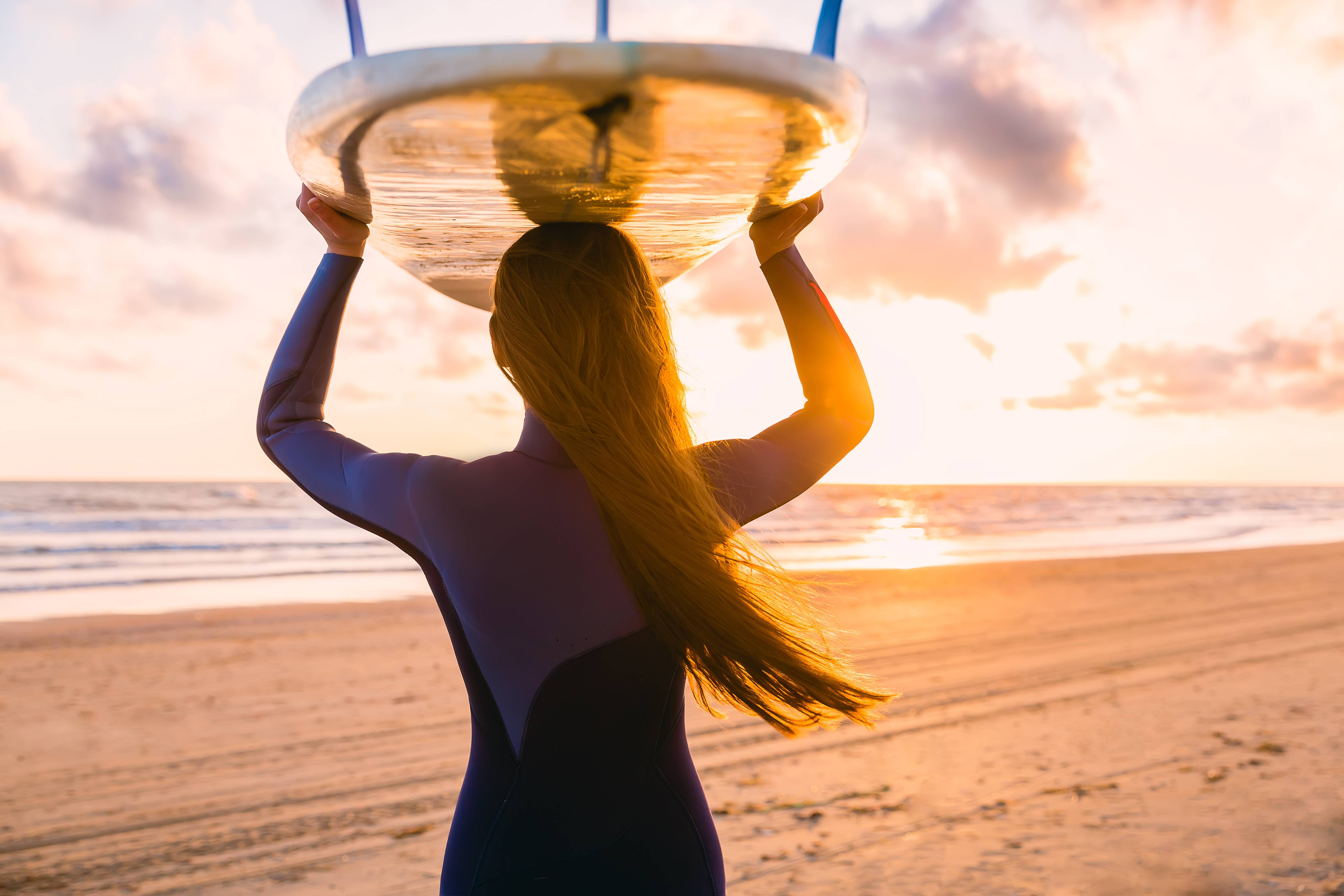 ragazza con tavola da surf sulla testa al tramonto