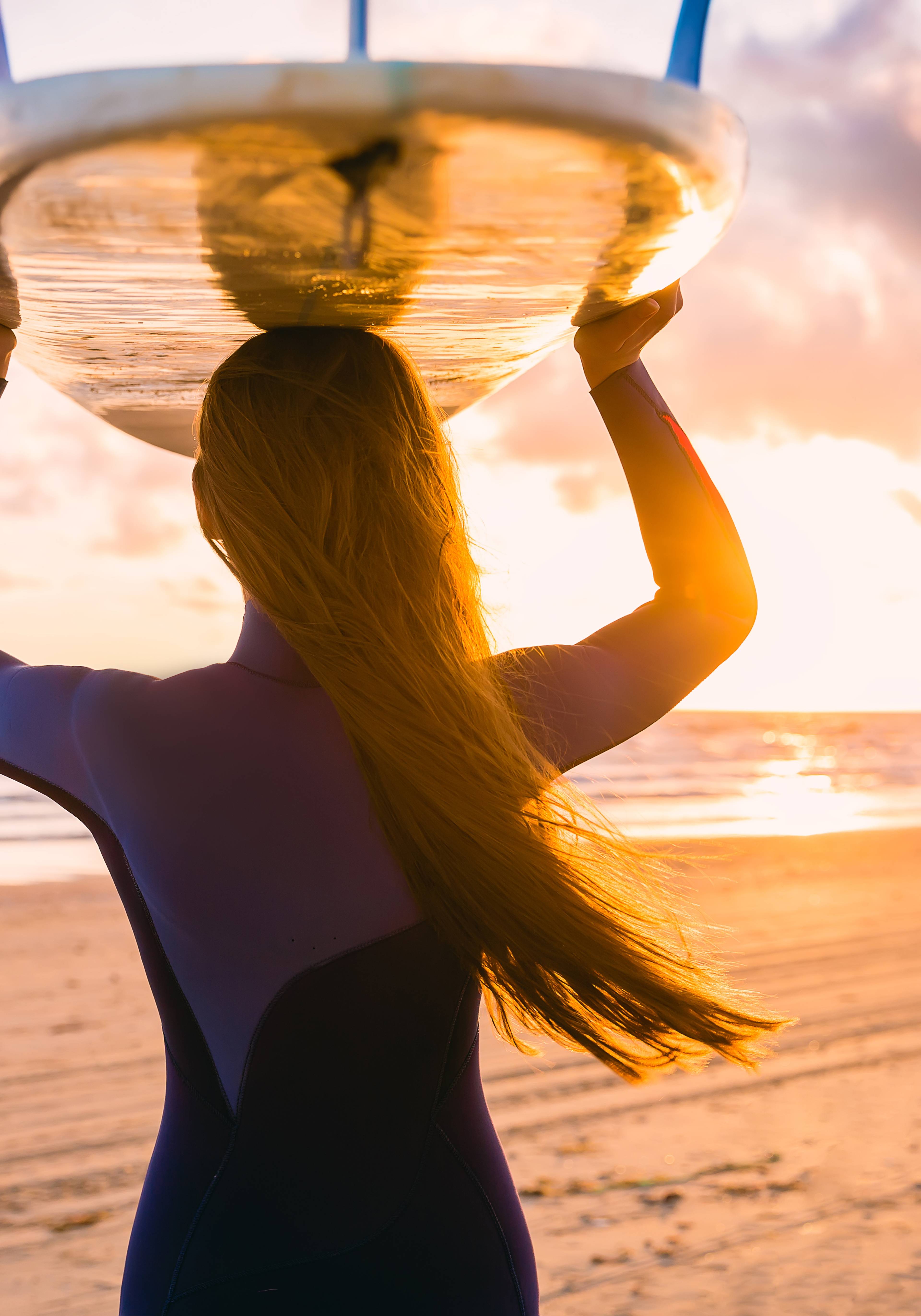 ragazza con tavola da surf sulla testa al tramonto