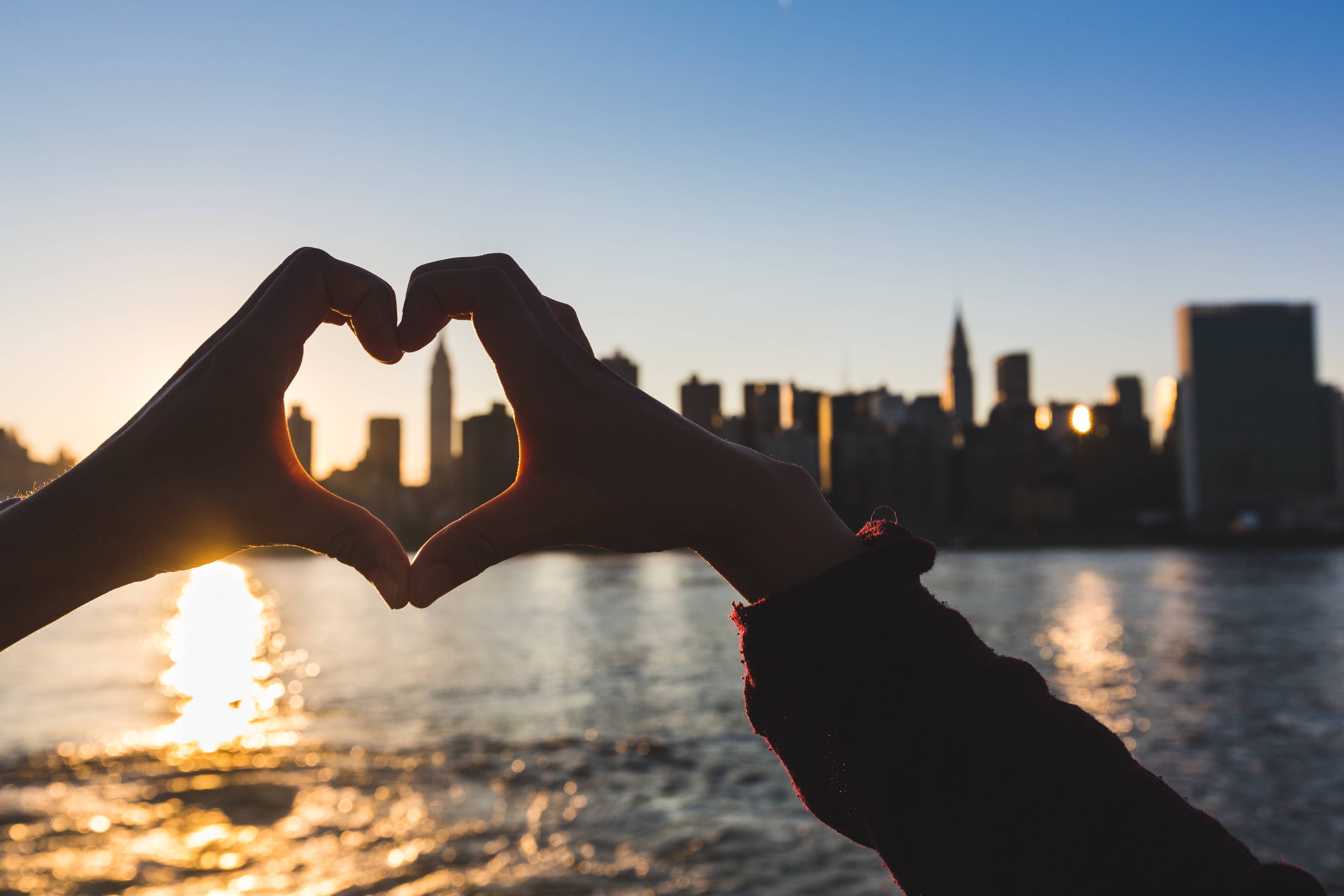 mani a forma di cuore davanti allo skyline di new york city al tramonto