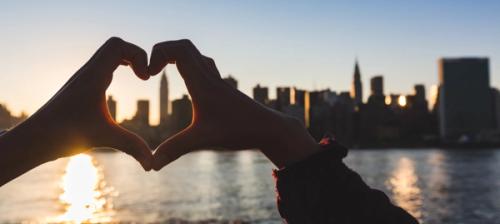 mani a forma di cuore davanti allo skyline di new york city al tramonto