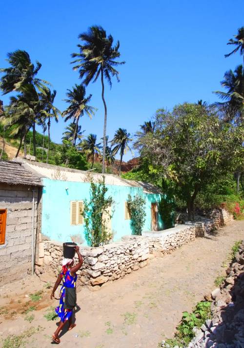 donna trasporta acqua sulla testa in un villaggio colorato