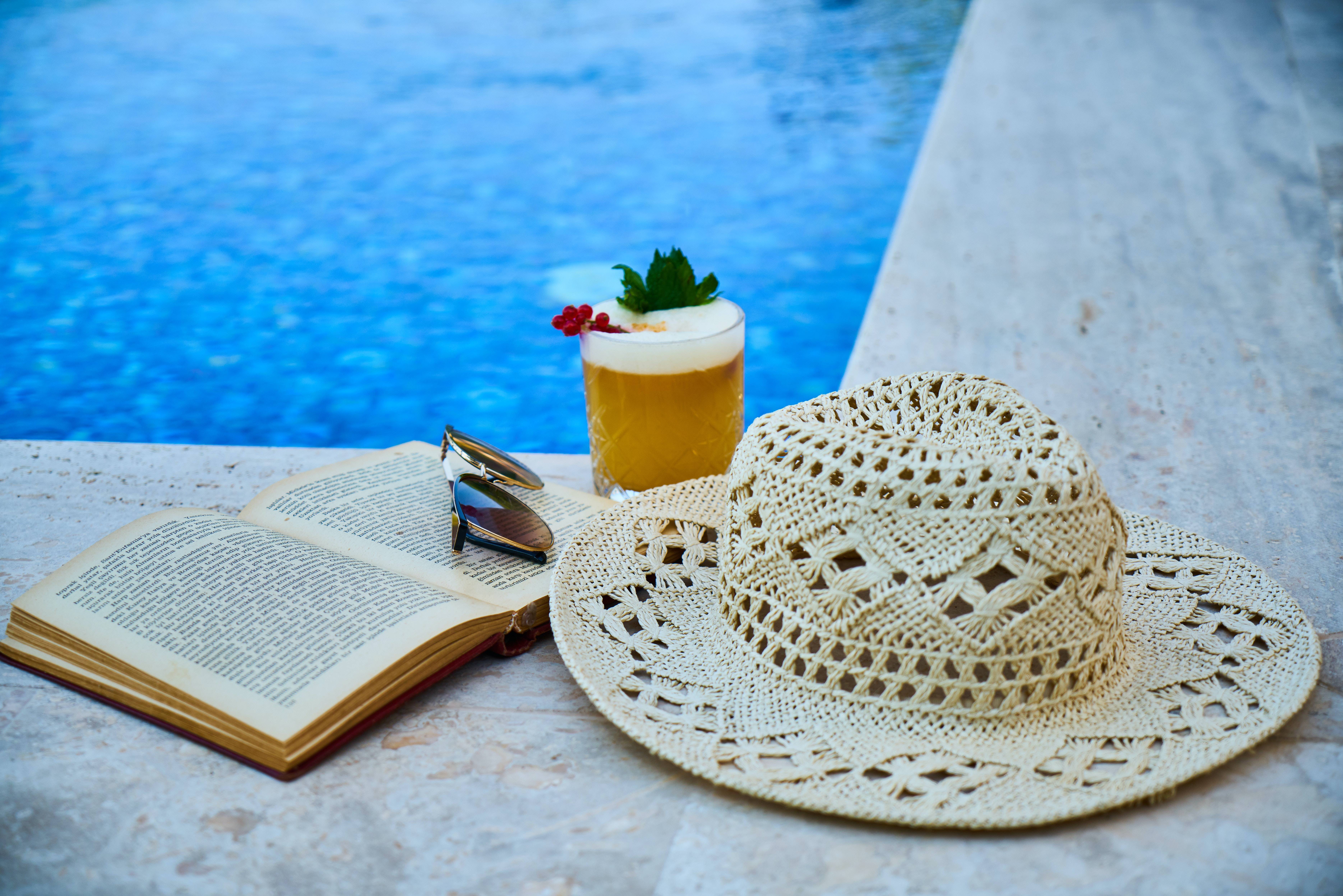 libro con cappello e cocktail a bordo piscina