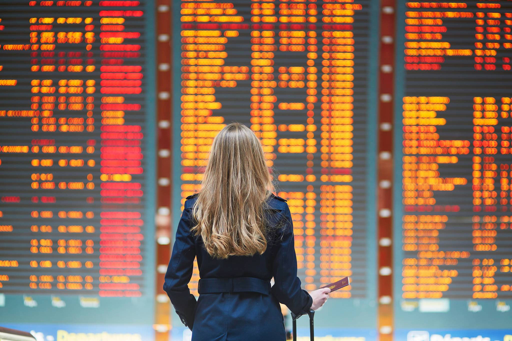 donna bionda con valigia davanti a tabellone voli aeroporto