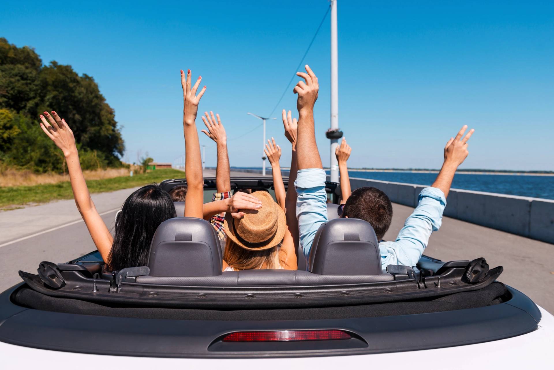persone in viaggio in macchina senza tettuccio con braccia alzate