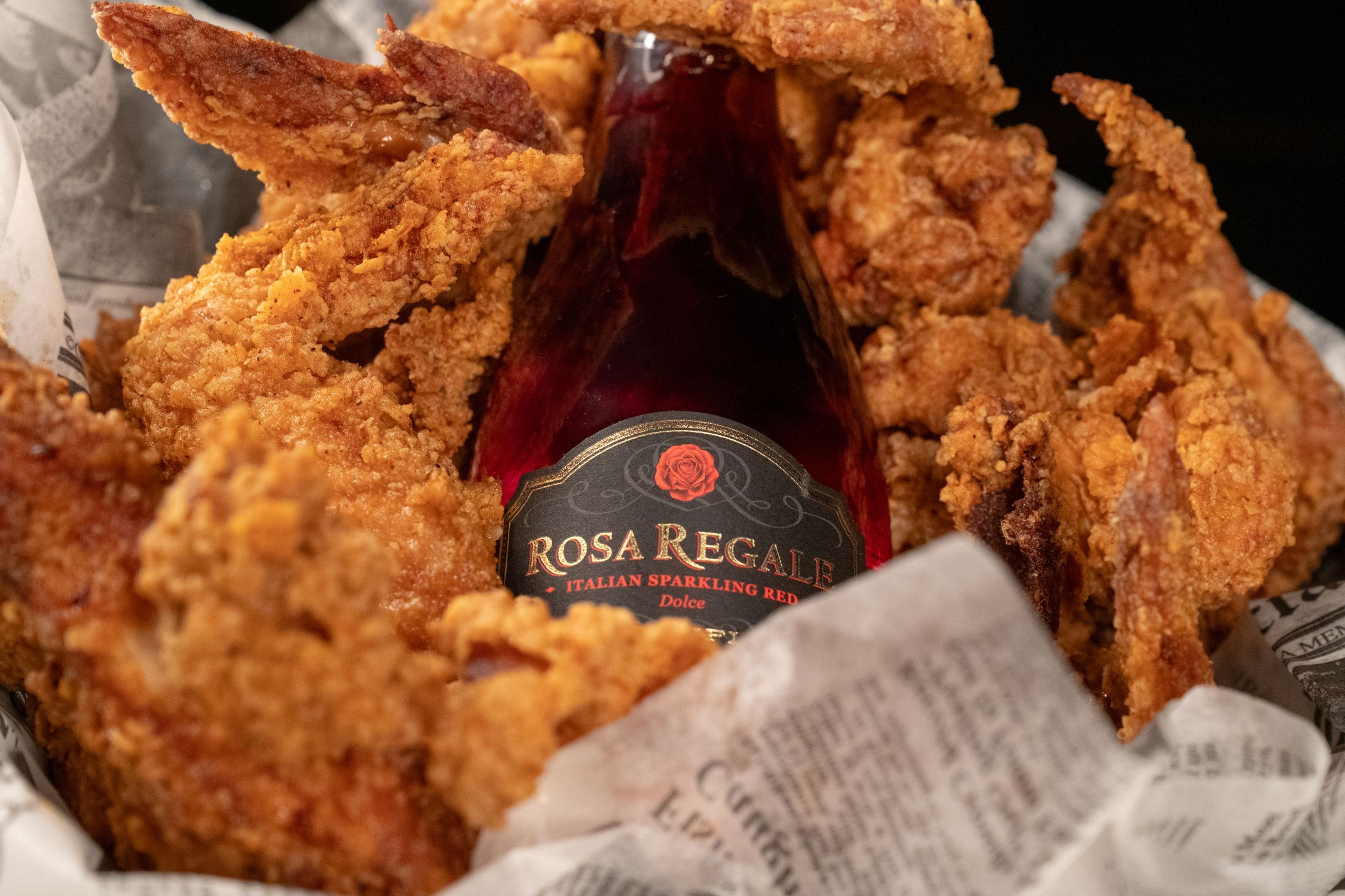 A basket of fried chicken in paper with a bottle of Rosa Regale sparkling wine