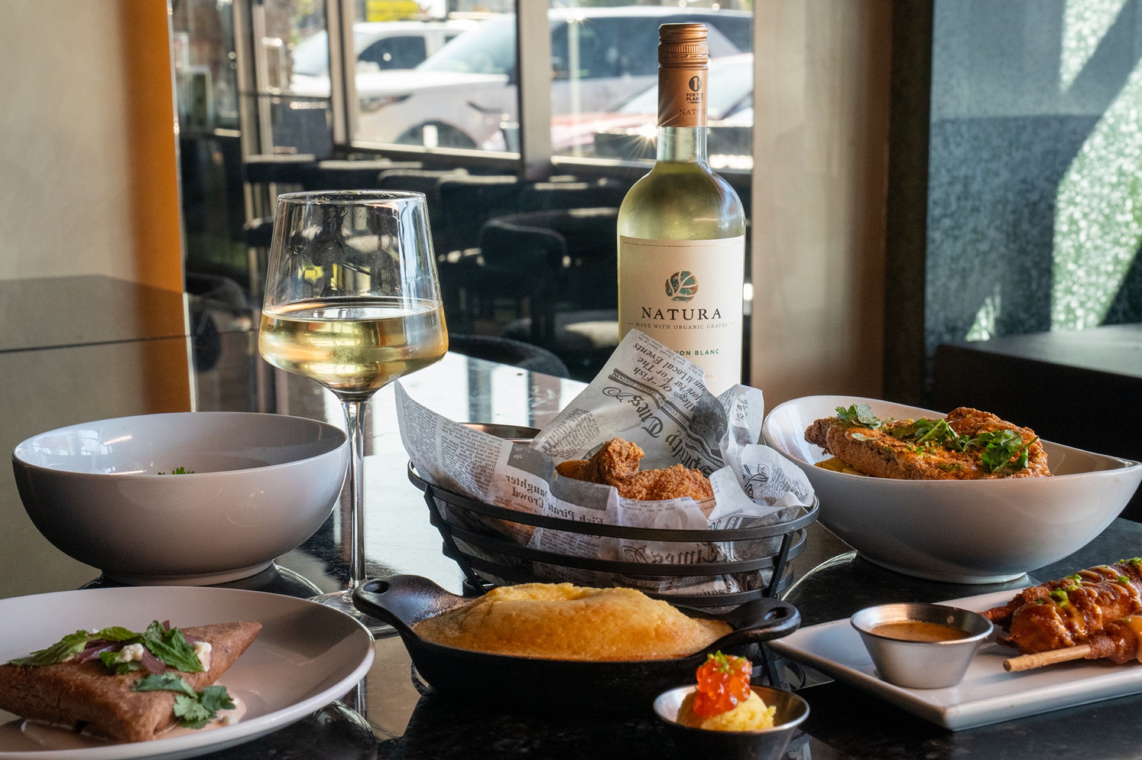 A table of shared plates with a glass and bottle of white wine