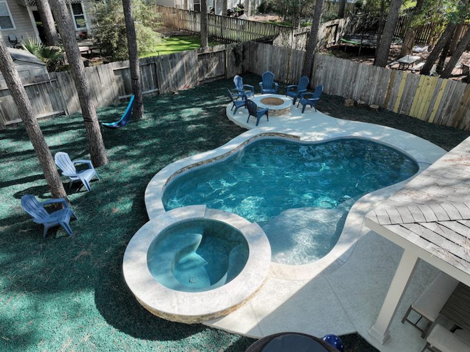 Gunite-style freeform pool with attached raised spa, stone veneer, and light coping
