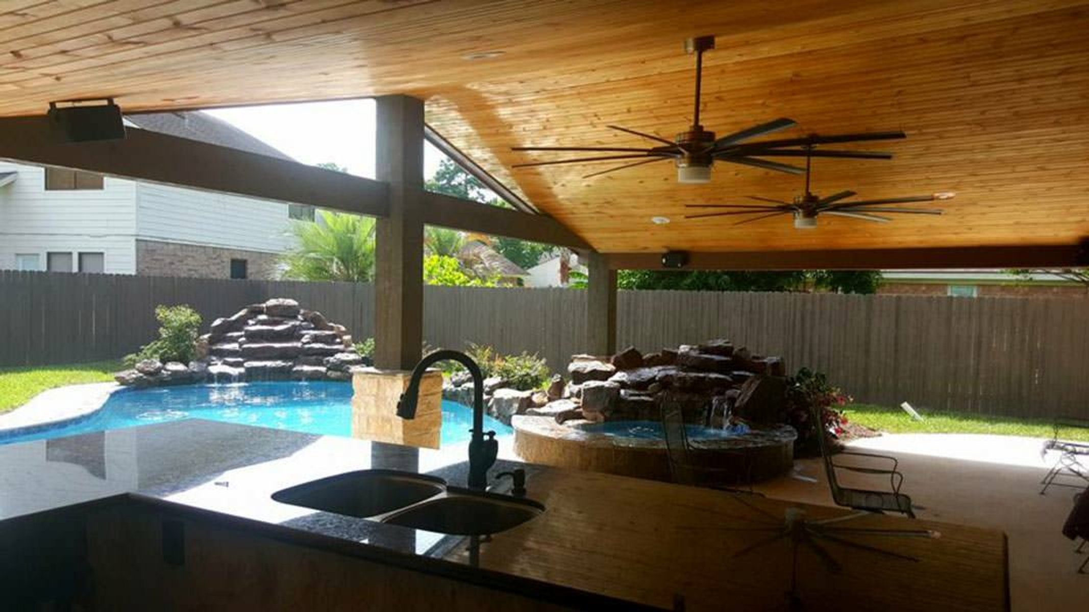 Spacious outdoor living area with wooden ceiling, large fans, and a pool
