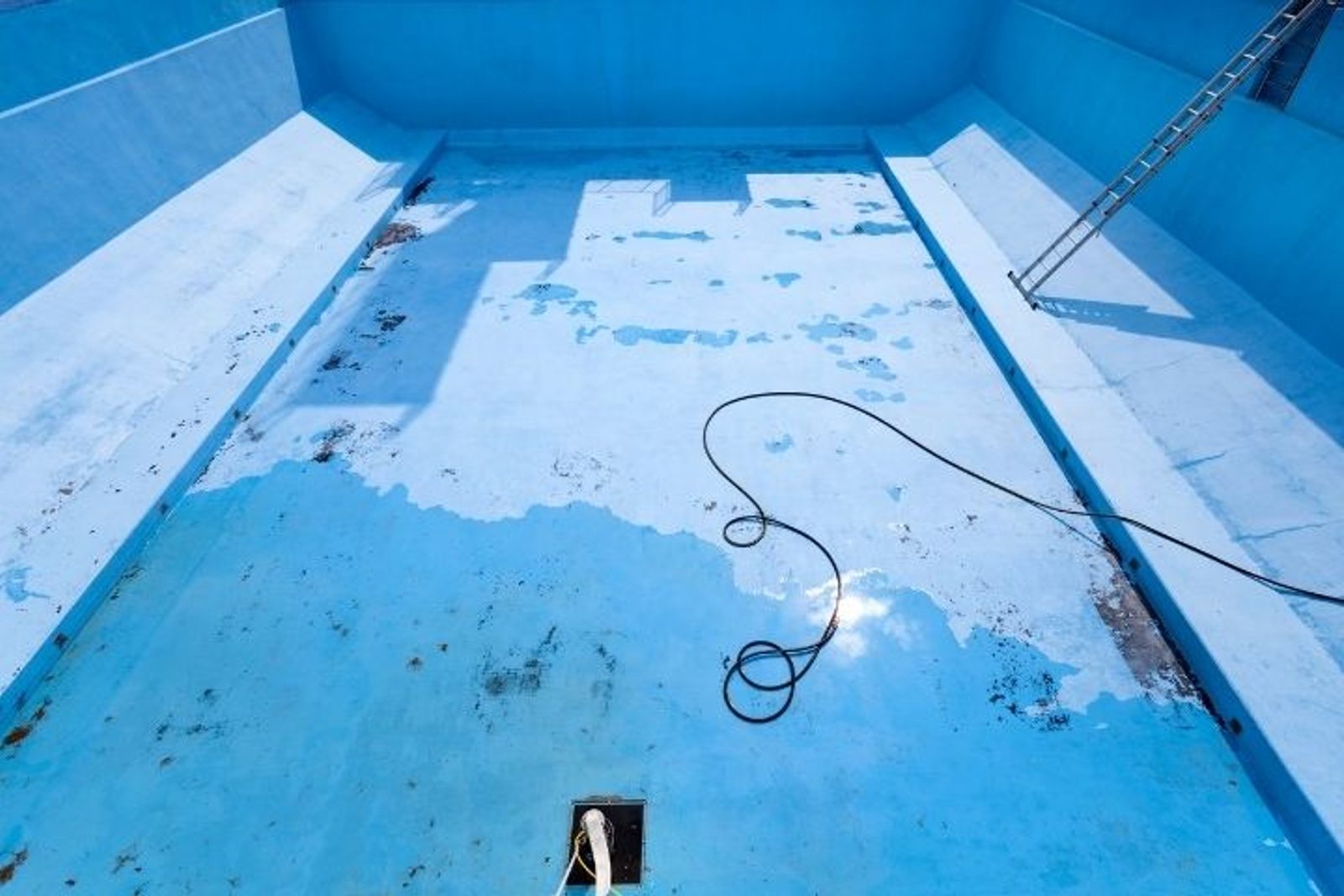 Drained swimming pool with worn and peeling interior surface ready for renovation