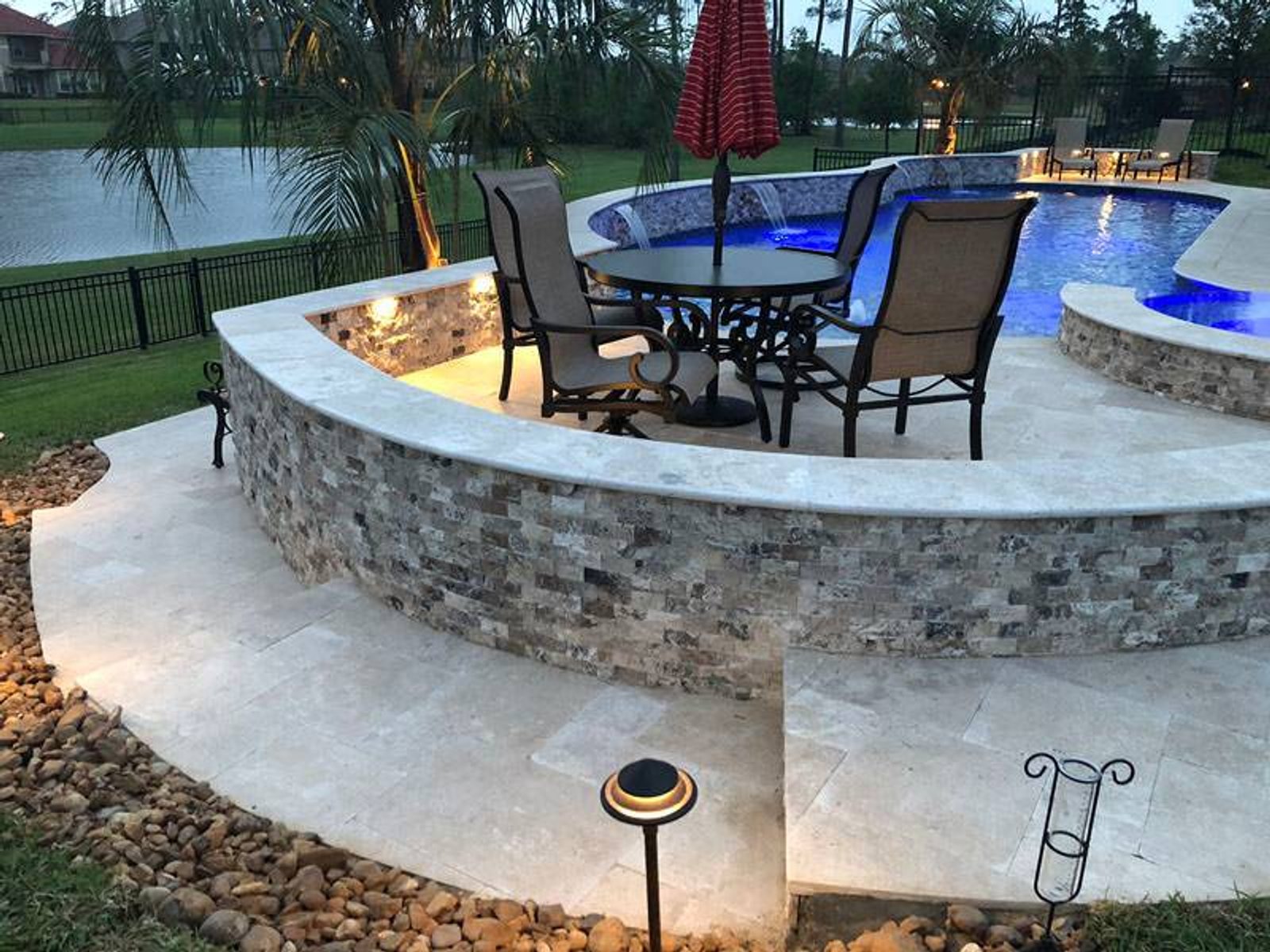Elevated custom outdoor patio with a round dining table, chairs, and umbrella overlooking a swimming pool