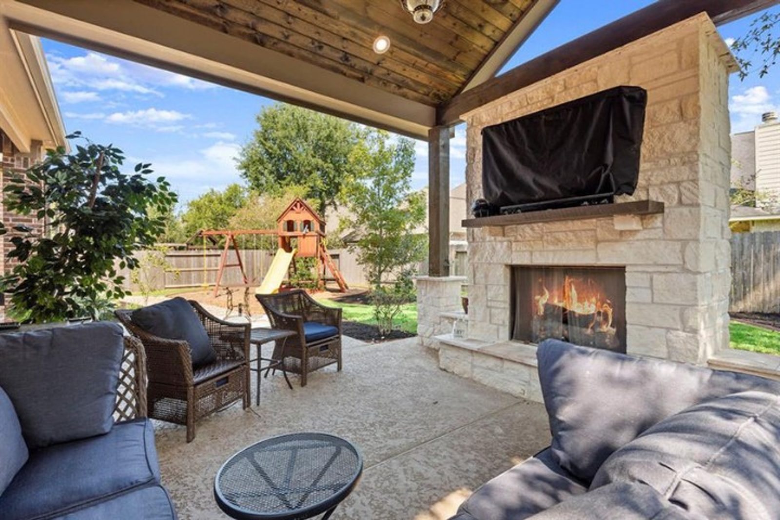 Outdoor living space featuring a timeless stone fireplace, cozy seating, and a structured entertainment zone