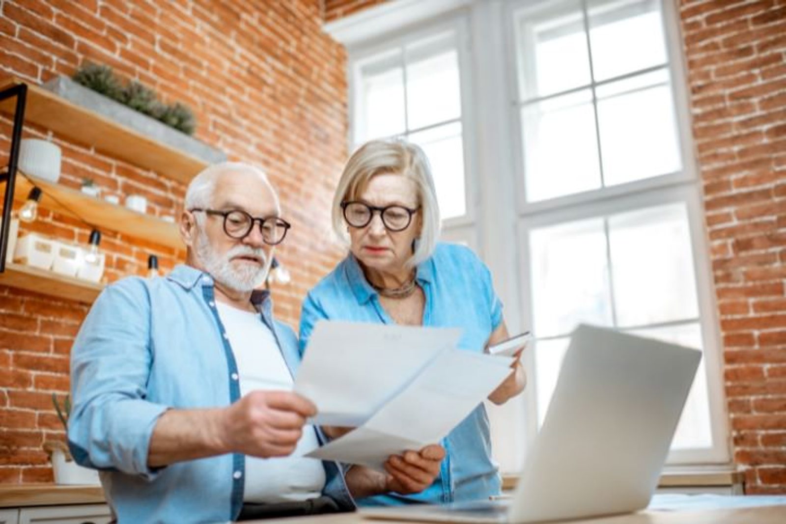 Senior couple discussing pool construction proposals and contractor qualifications while looking at documents and a laptop