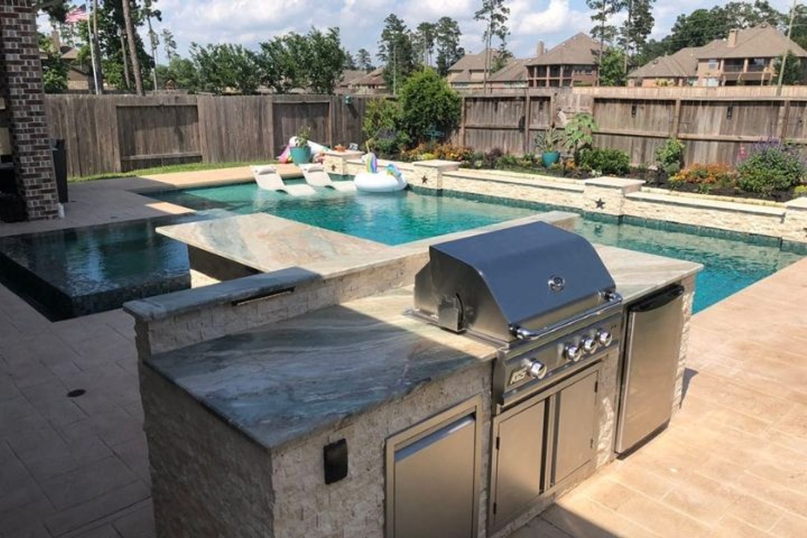 Custom outdoor kitchen with grill and stone countertops integrated into a poolside outdoor living area