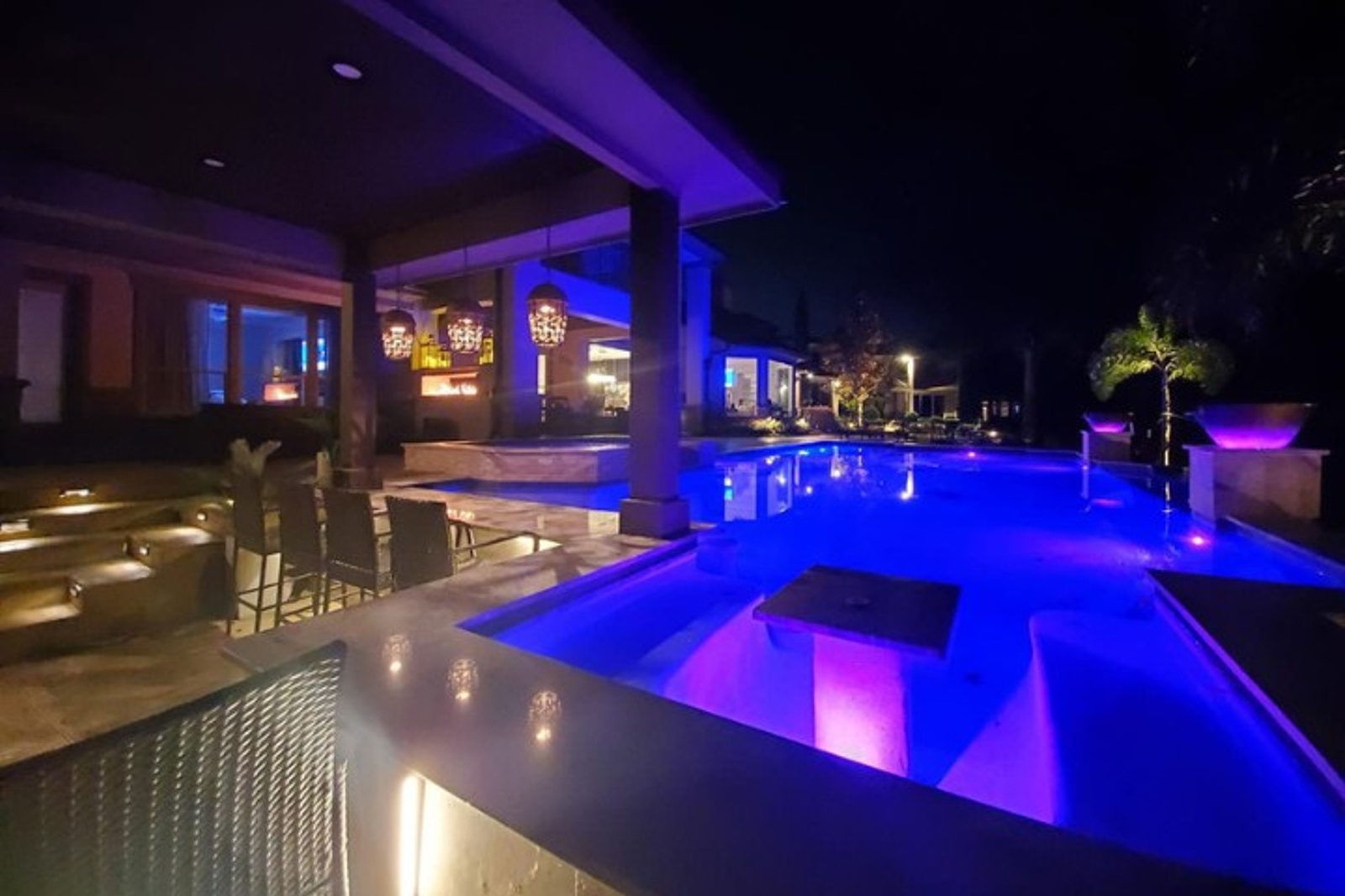 Automated underwater pool lights brighten the swim area near a covered patio