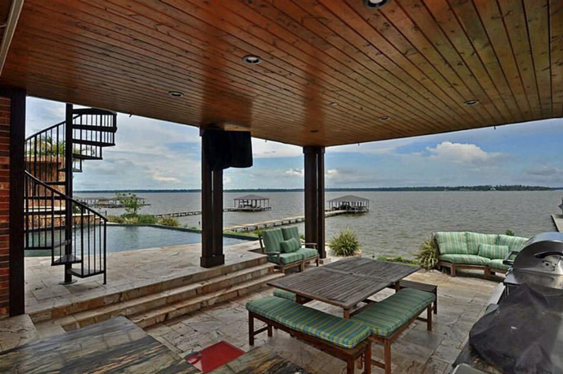 Covered outdoor patio featuring a spiral staircase, wooden ceiling, and lakefront view