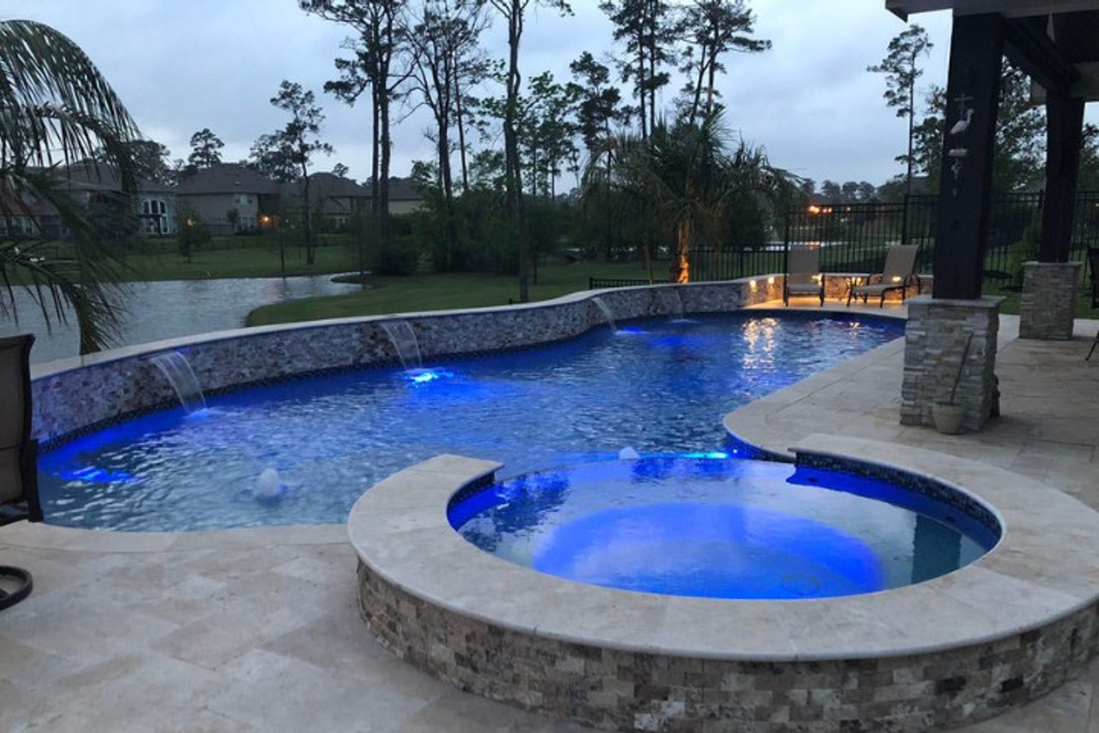 Illuminated pool and spa combo with modern landscaping and greenery