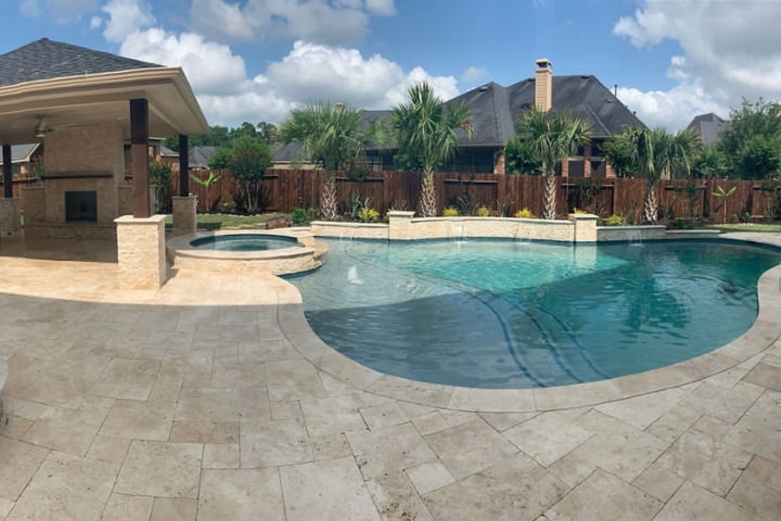 Elegant pool and spa surrounded by travertine pavers in a stylish backyard setting