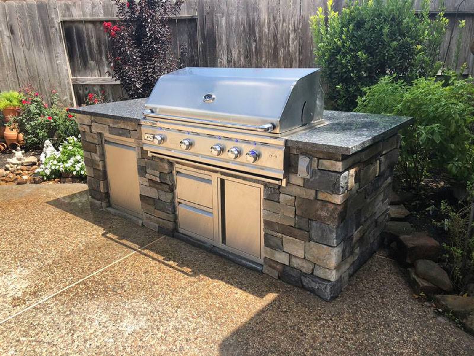 Houston backyard stone outdoor kitchen featuring a stainless steel grill and granite countertop