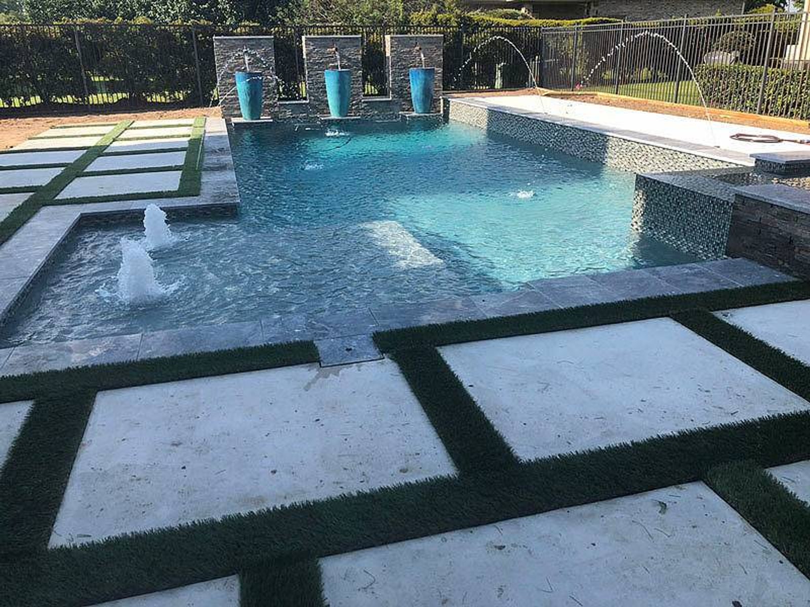 Contemporary geometric swimming pool with integrated fountains, tiled deck, and elegant landscaping