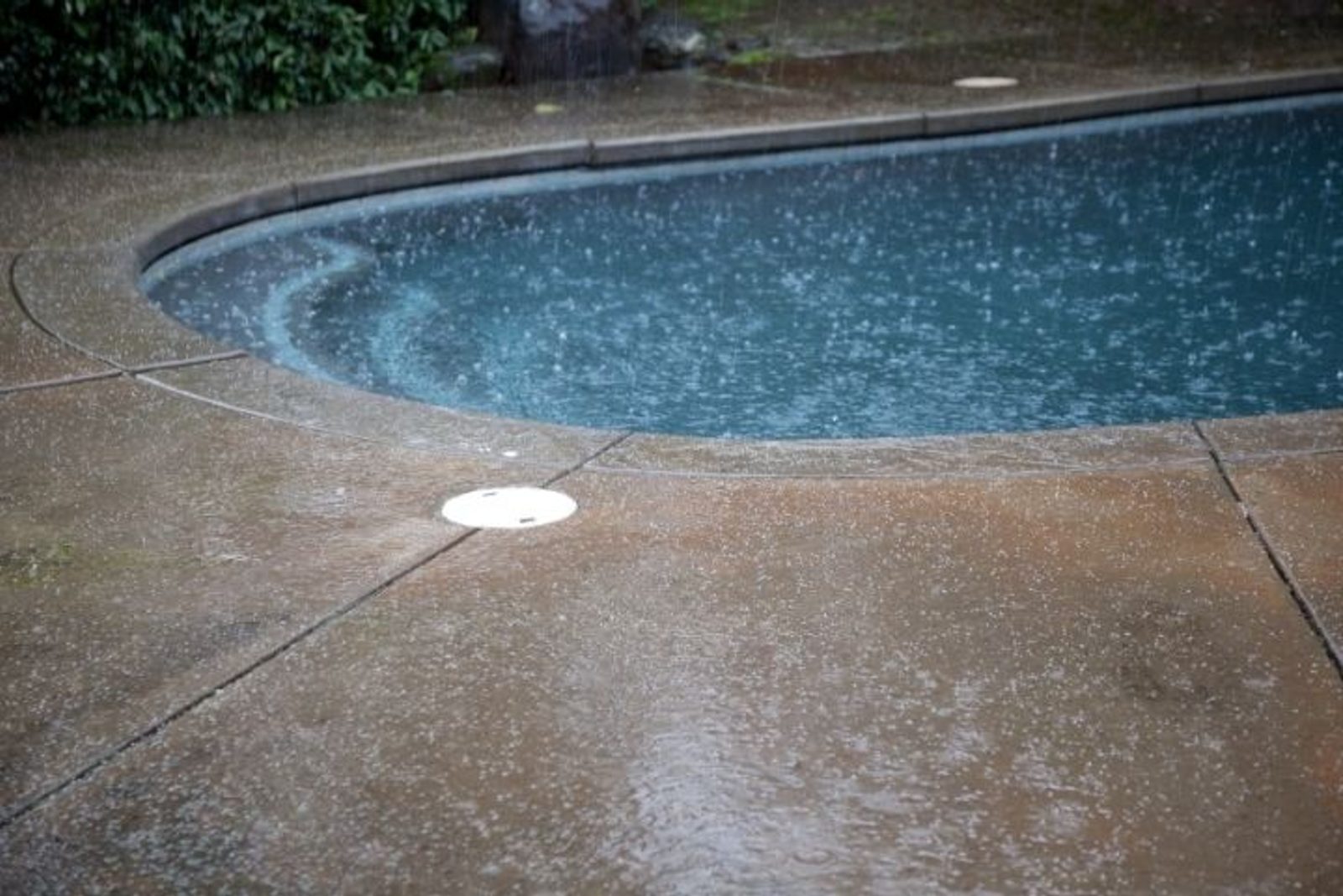 Heavy rain falling on a backyard swimming pool and surrounding deck