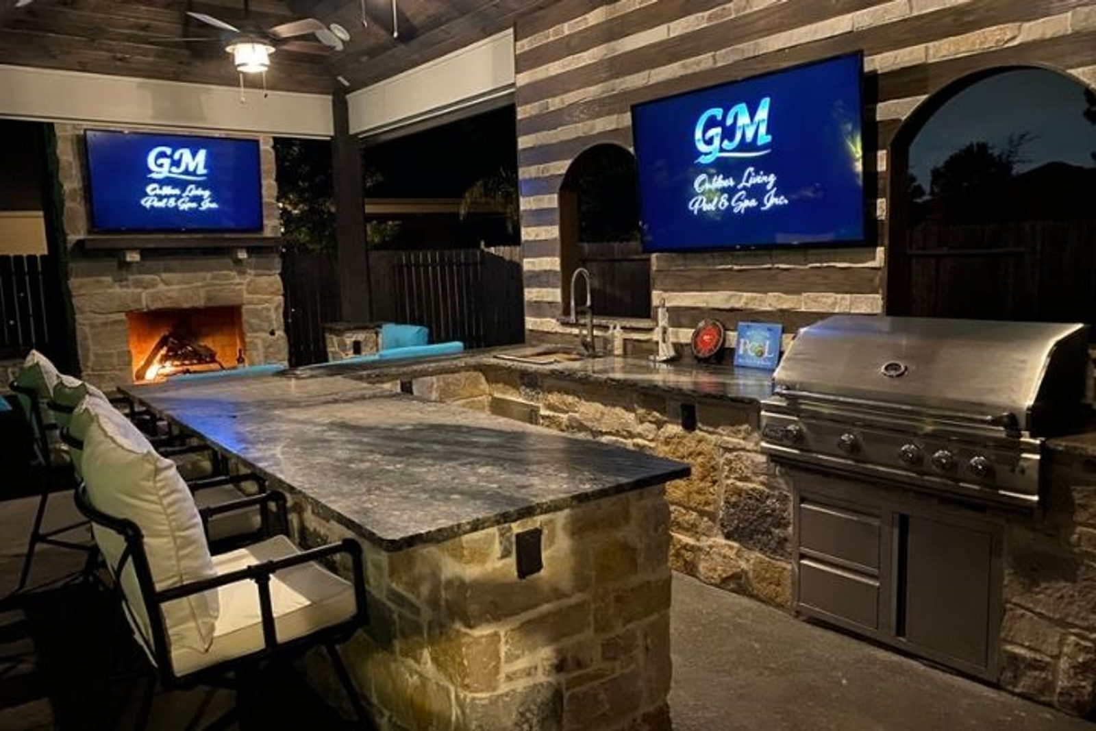 Custom covered outdoor kitchen by GM Outdoor Living, Pool & Spa with built in grill, sink, island, and fireplace