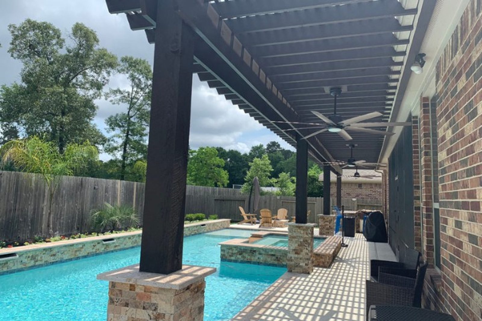 Pergola made from dark wood with ceiling fans, offering shade along a modern pool