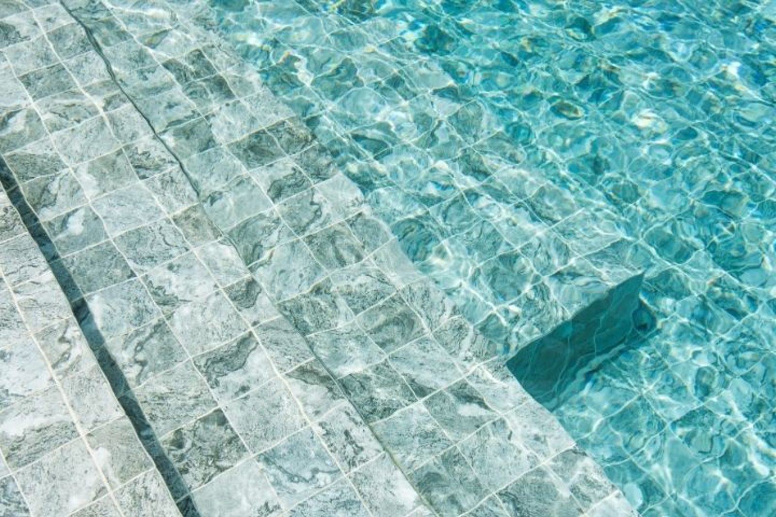 Light stone tile pool finish beneath clear water