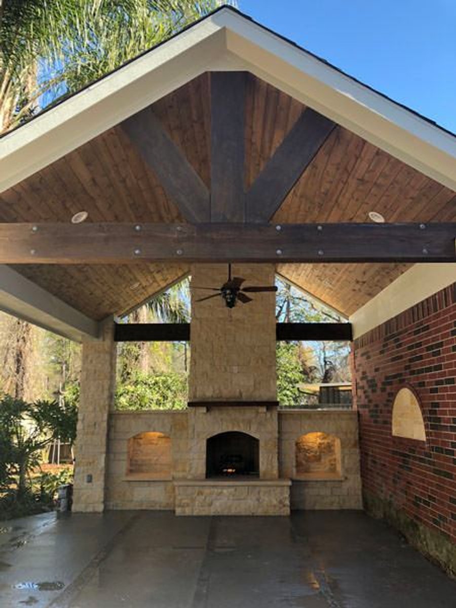 Covered patio with a central stone fireplace, built-in lighting, and brick wall accents