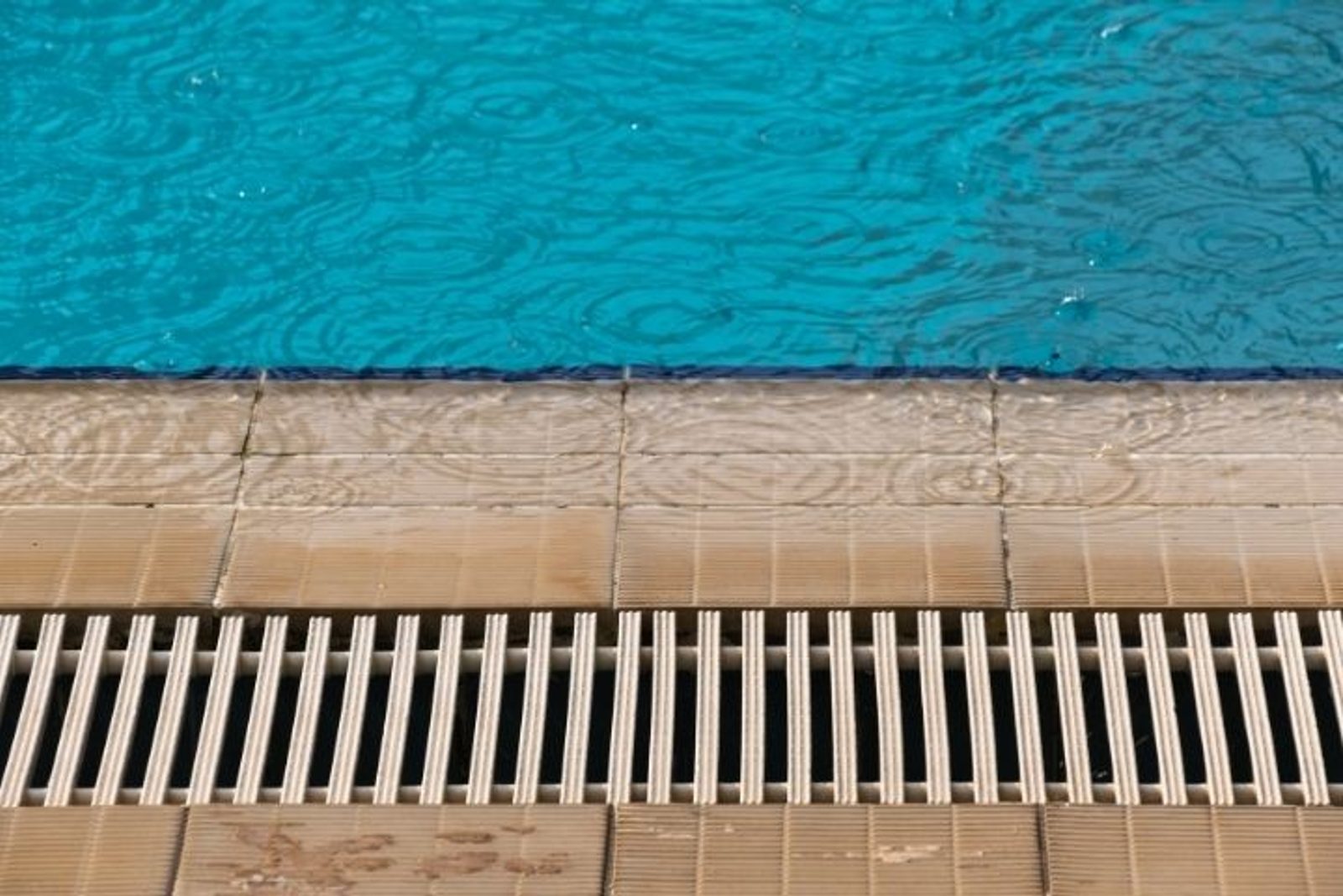 Drainage grate between the swimming pool and surrounding patio surface