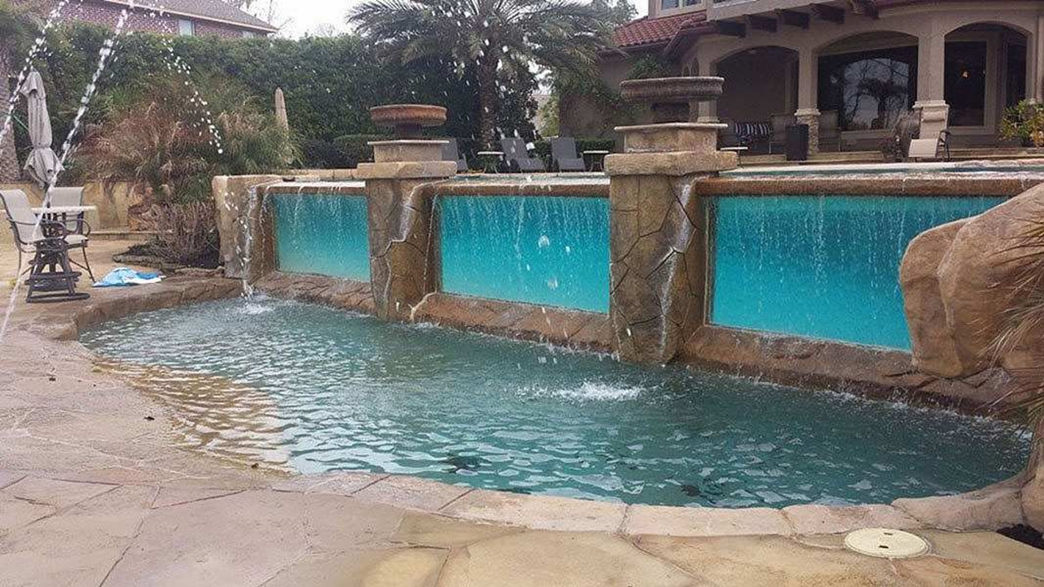 Custom-designed pool with elevated water features, rock formations, and integrated glass walls