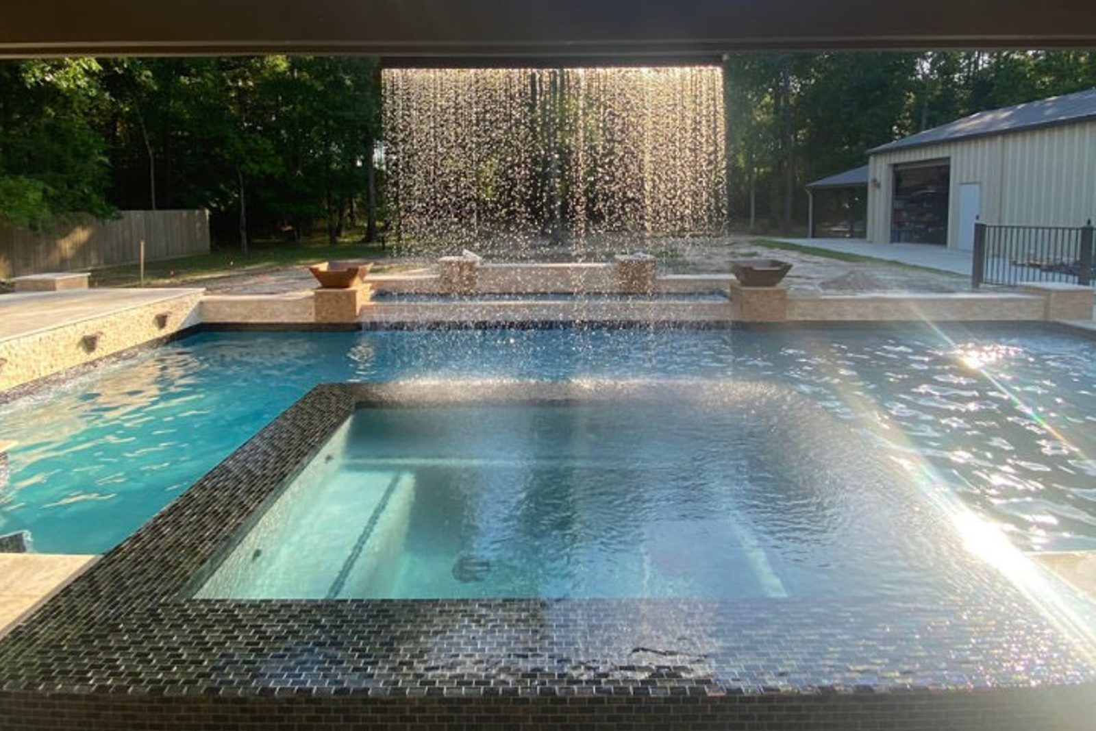 Raised spillover spa with waterfall feature flowing into an inground pool
