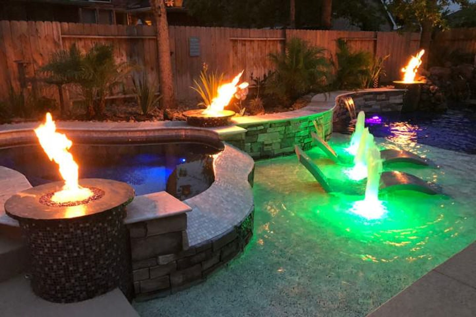 Luxury pool with stunning lighting, fire features, and water jets at night