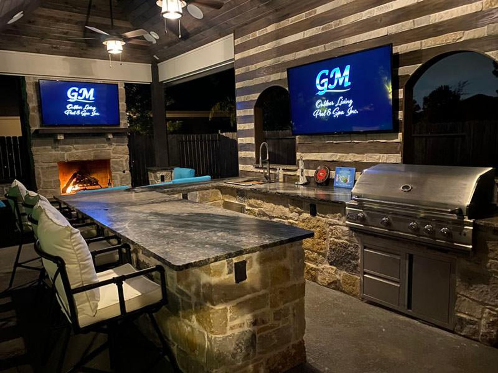 Luxury outdoor kitchen in Houston with double TV setup, fireplace, and premium stainless steel grill