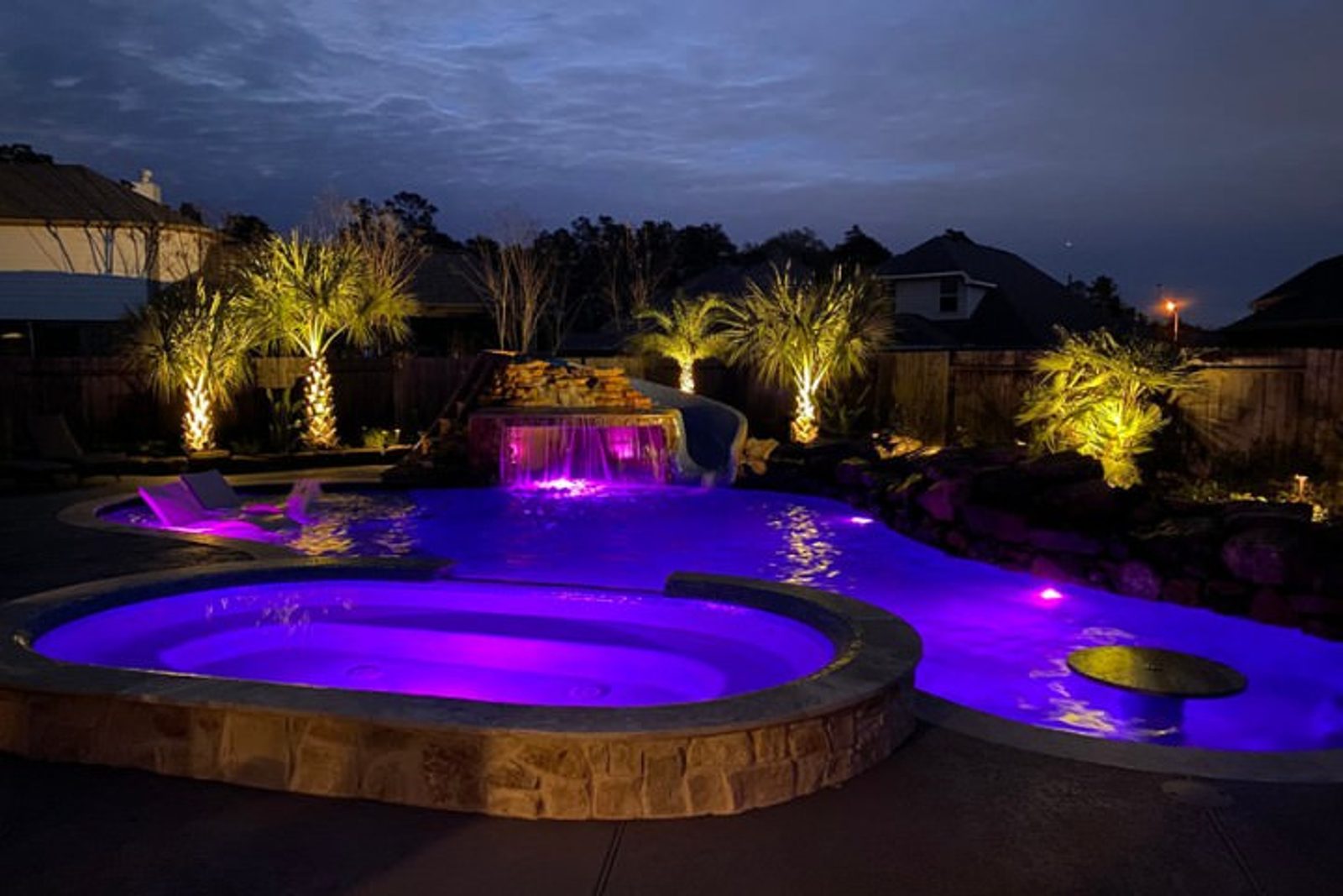A modern pool design with a spa spillover and LED lighting water features